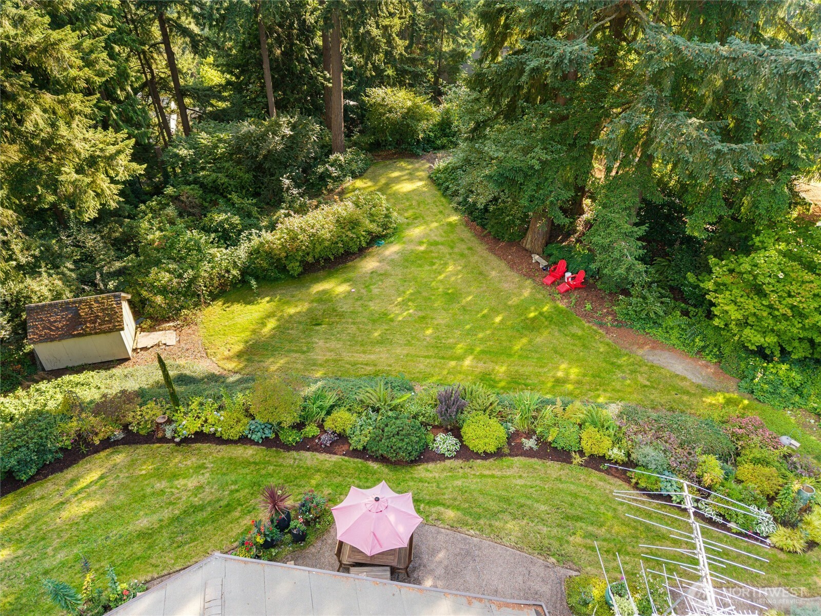 Aerial backyard with a broad lawn, mature trees, garden beds, a shed, and patio seating.