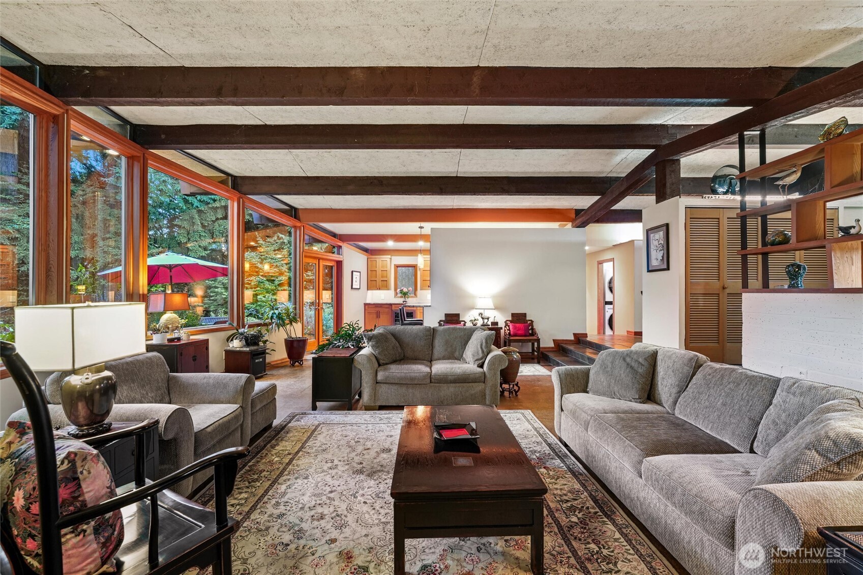 Living room with gray sofas, exposed ceiling beams, and large windows overlooking trees.