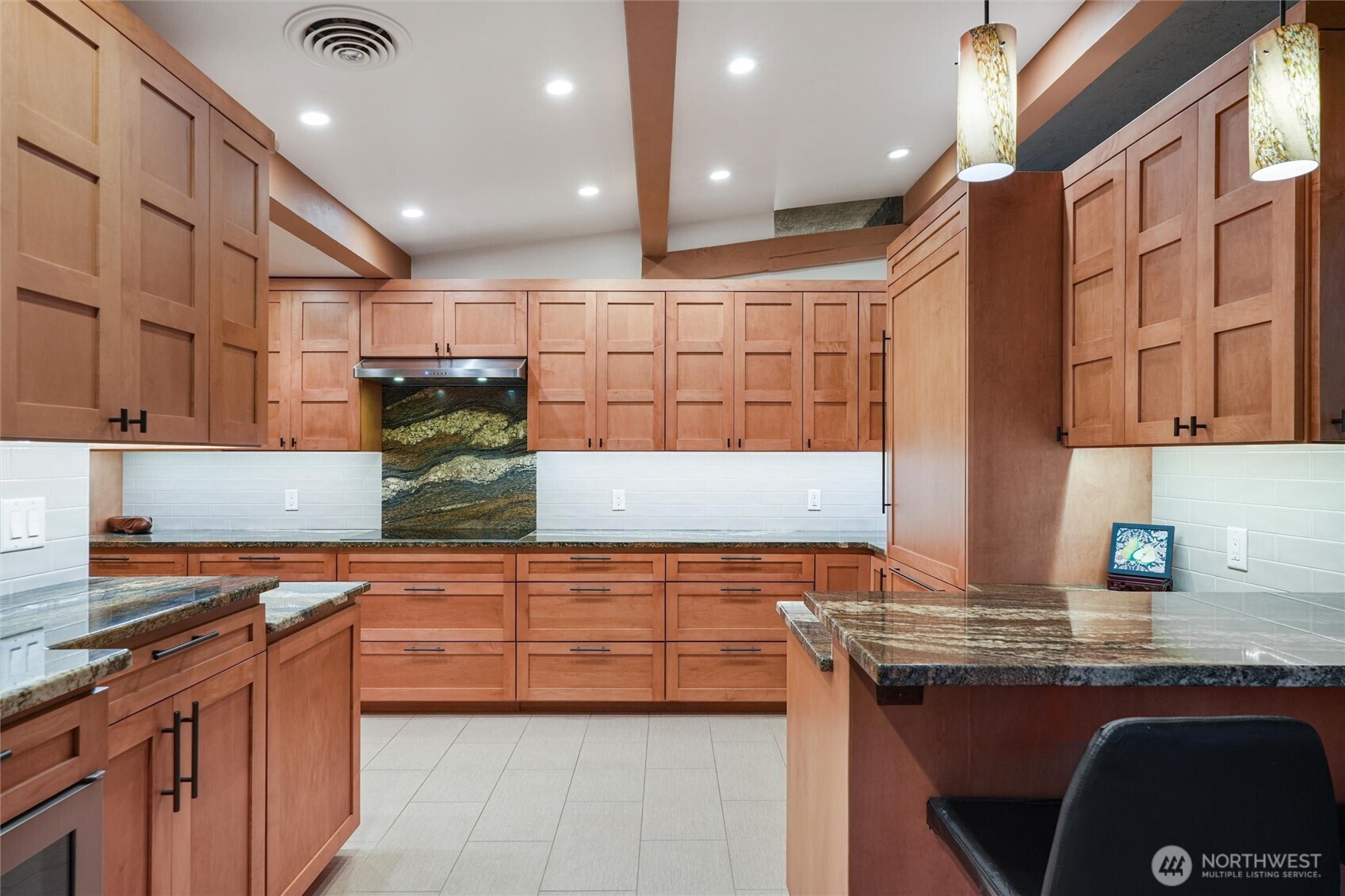 Kitchen with extensive wood cabinetry, polished stone counters, and a dramatic veined stone backsplash.
