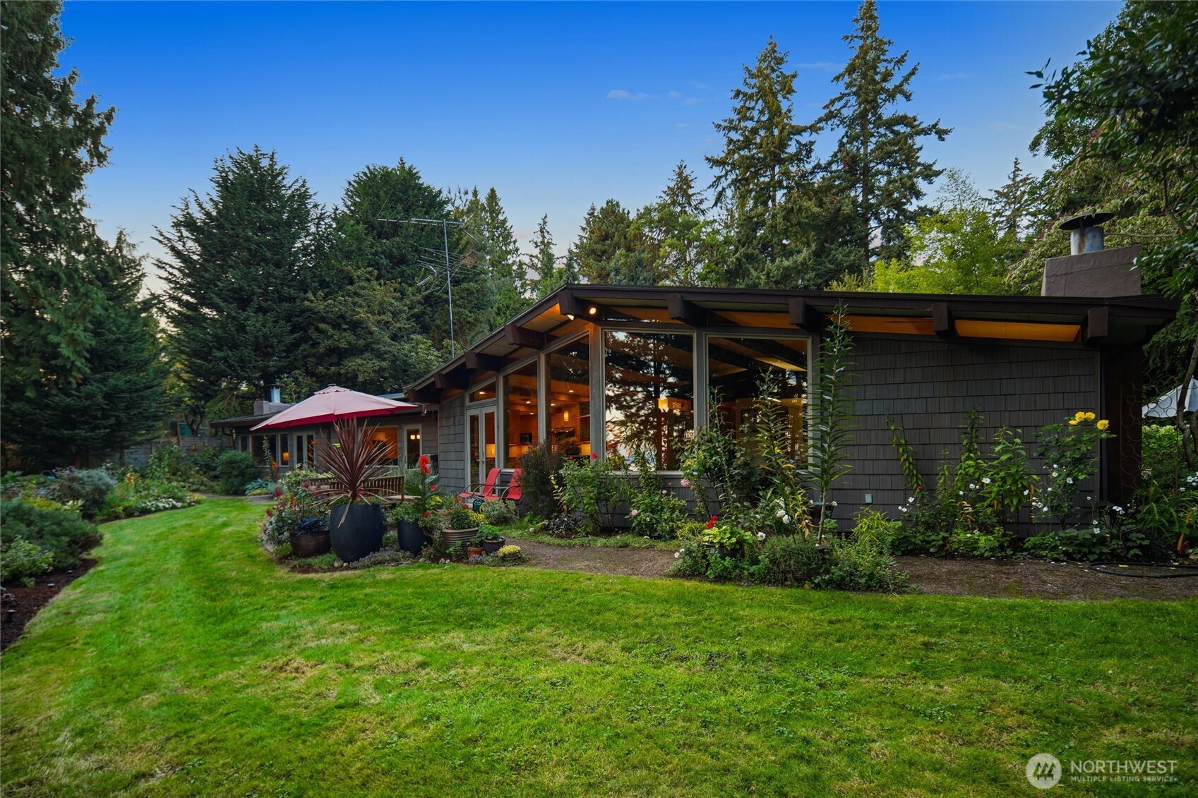 Low-profile home with a glass-fronted living area, landscaped garden, and red patio umbrella.