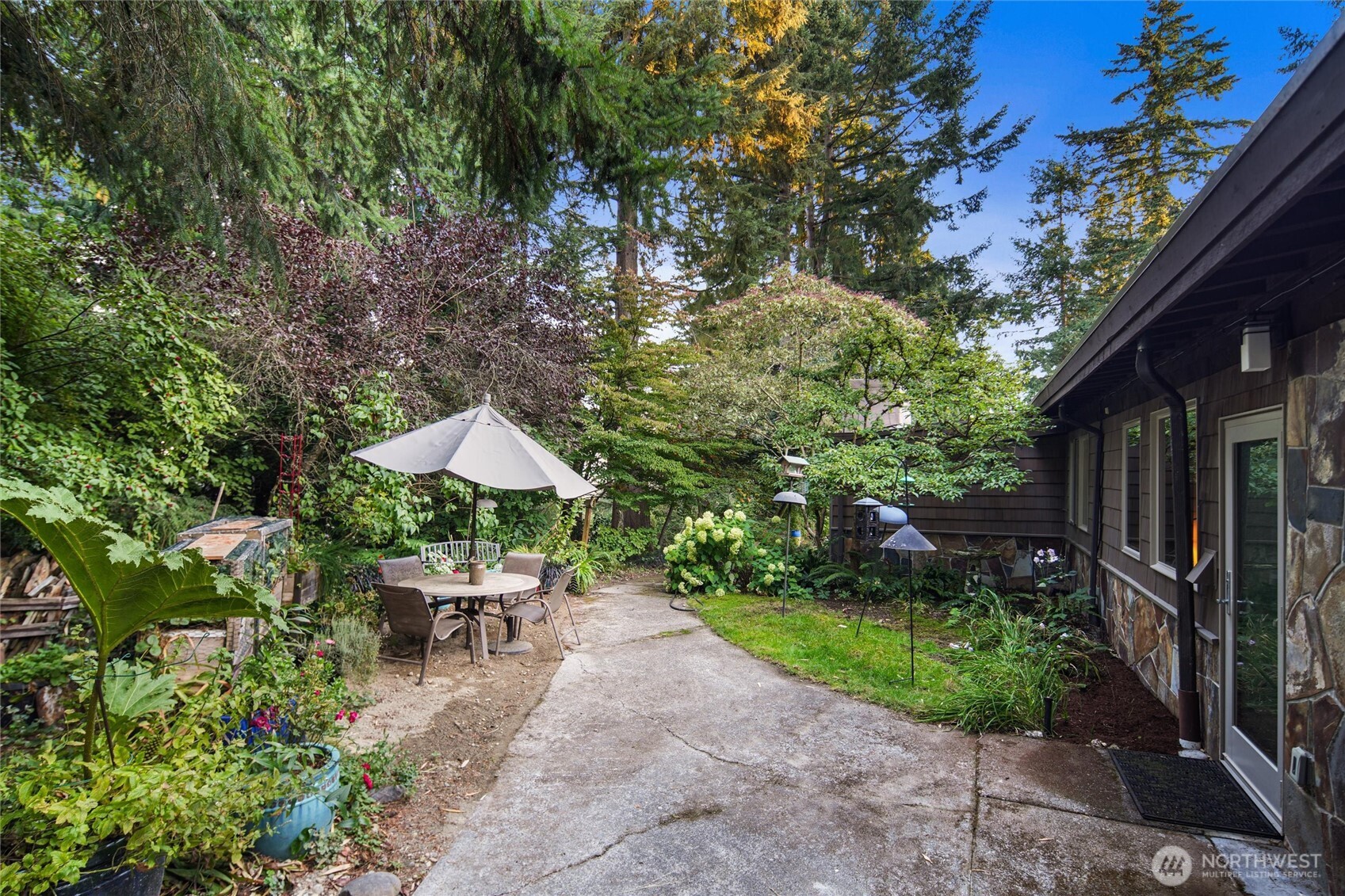 Landscaped backyard patio with an umbrella-shaded dining set beside the home.