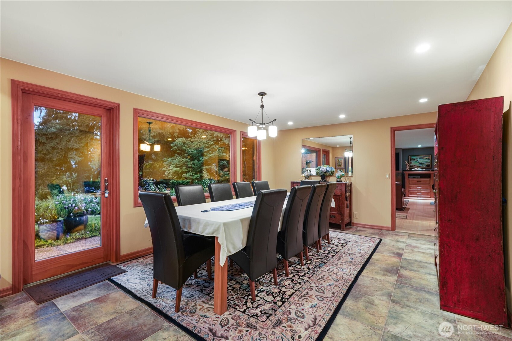 Dining room with a long table, dark chairs, garden-facing windows, and warm wood trim.