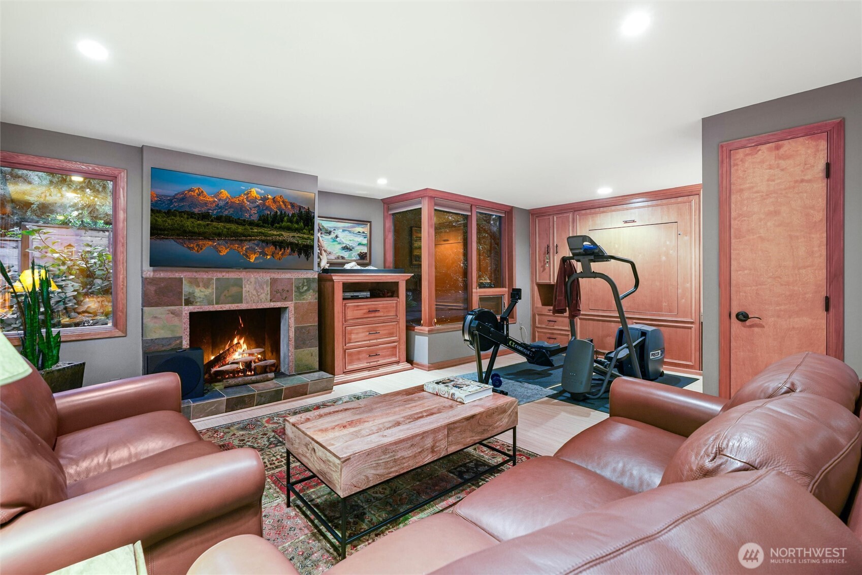 Furnished recreation room with leather seating, a stone fireplace, and exercise equipment.
