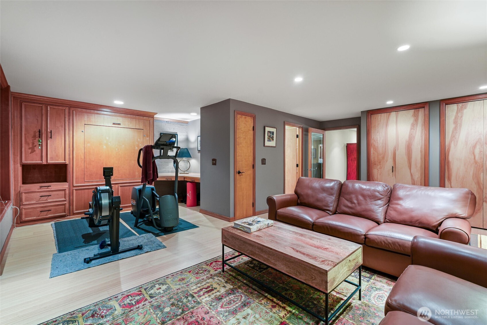 Living room and home gym with a leather sectional, wood cabinetry, and exercise equipment.