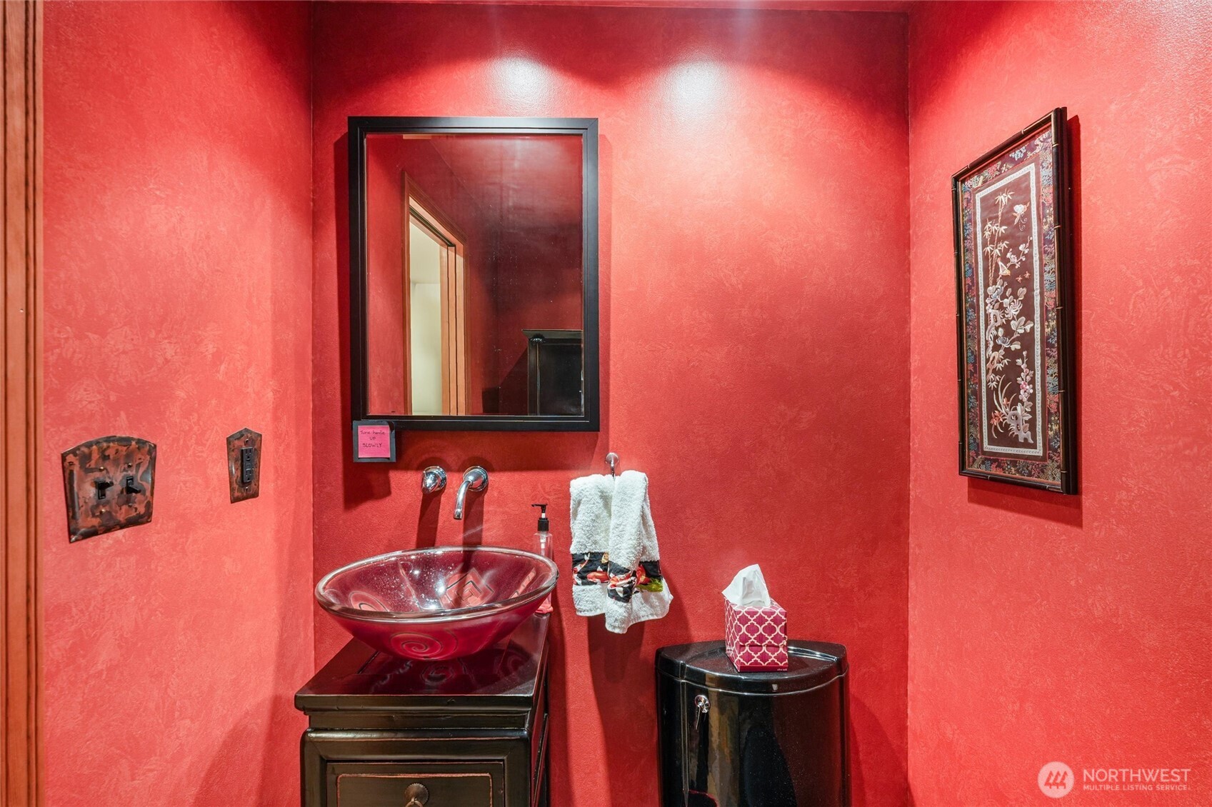 Powder room with vivid red walls, a glass vessel sink, and dark vanity.