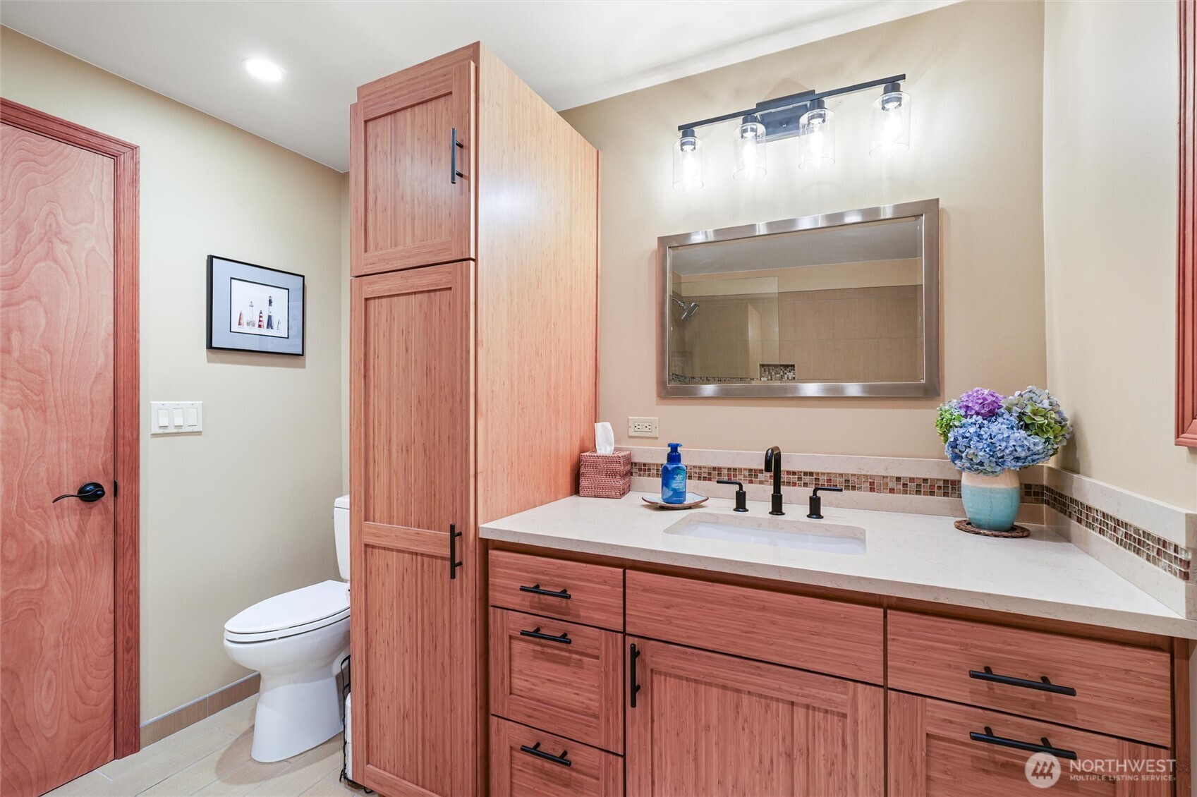 Bathroom with a long wood vanity, framed mirror, and hydrangeas on the counter.