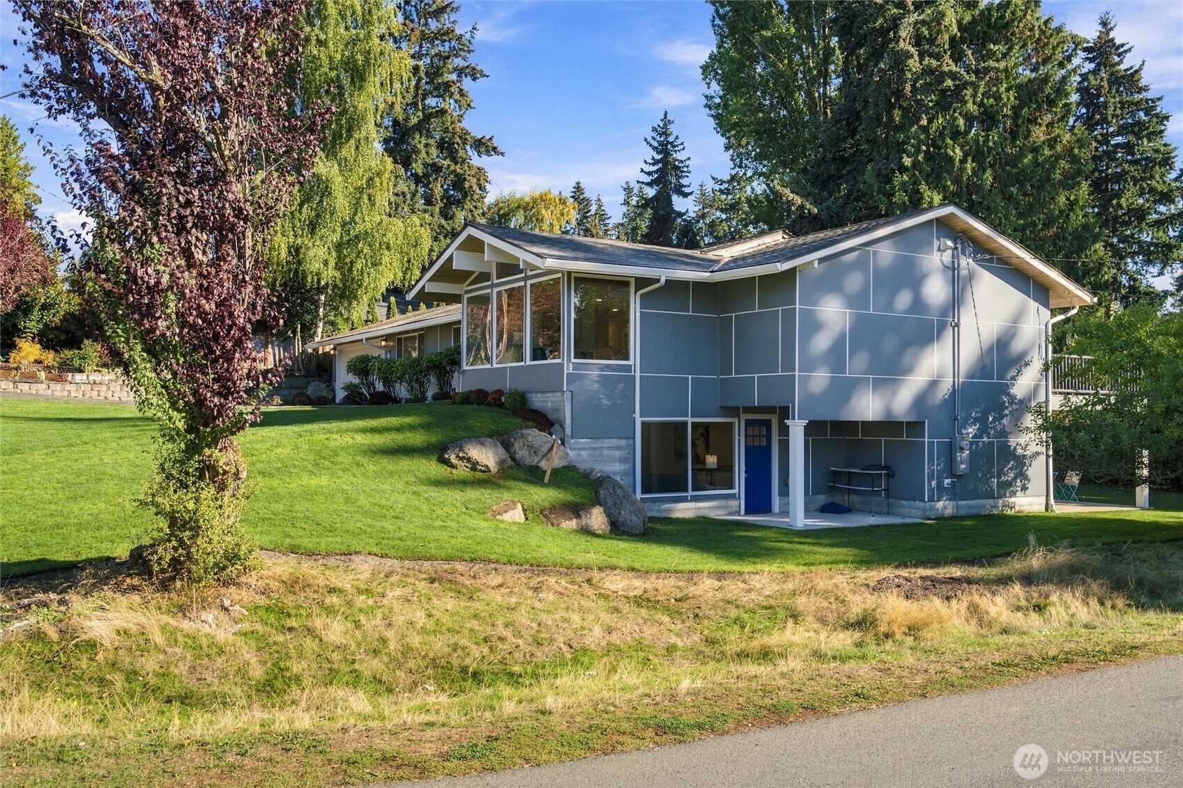 Blue-gray split-level home with a blue entry door, broad windows, and a landscaped lawn.