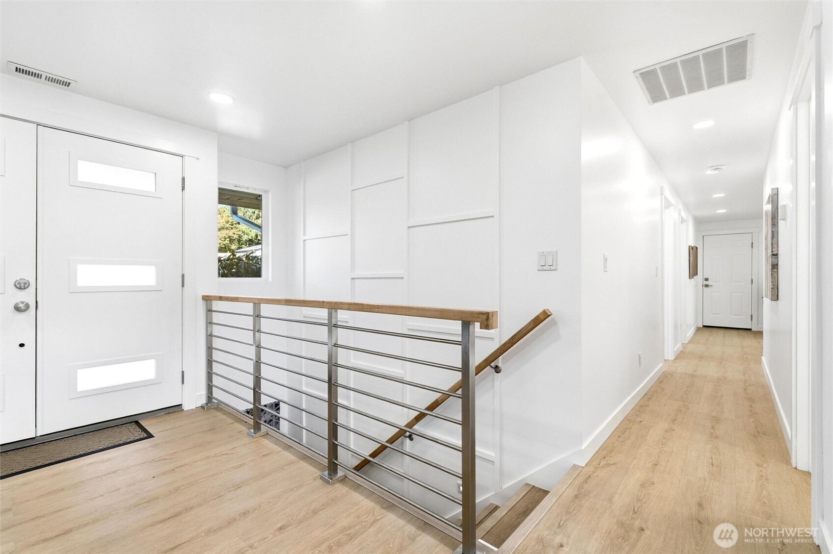 Entry hall with light wood floors, white paneled walls, and a metal railing around the stairwell.