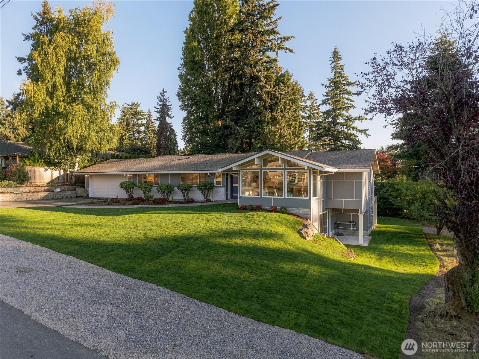 Gray home with a glass-fronted gable, attached garage, and broad lawn among mature trees.