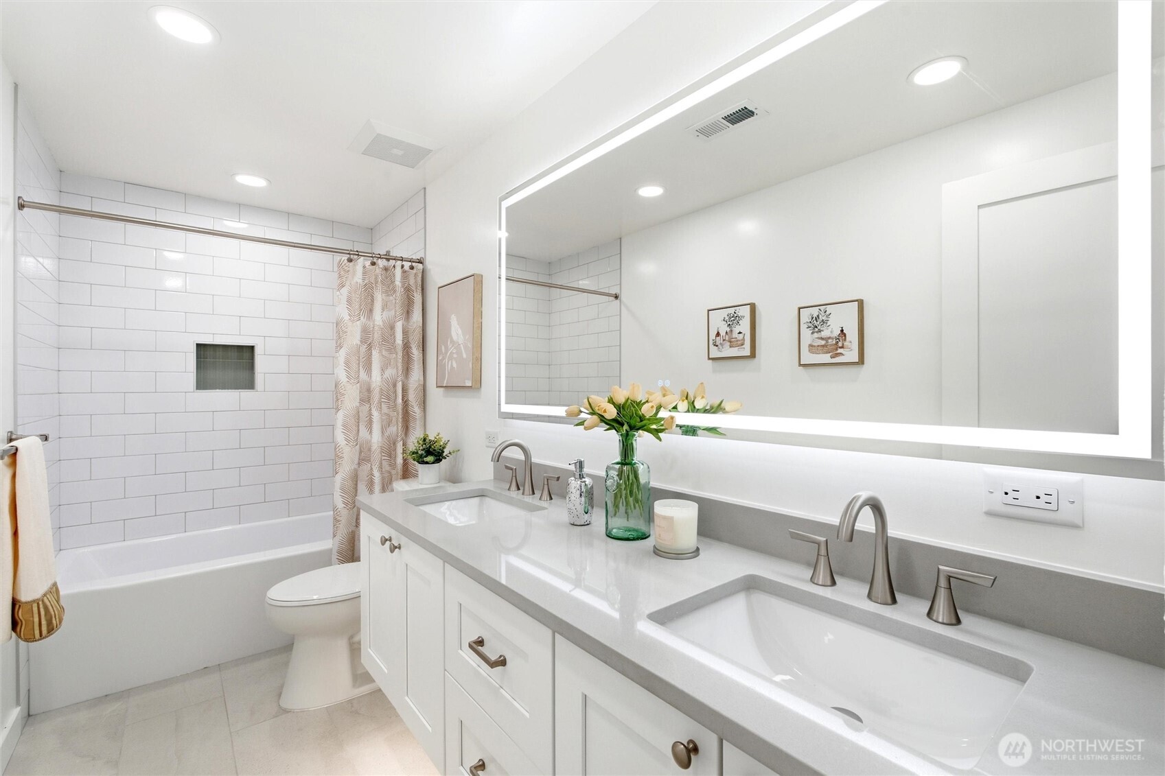 Bright bathroom with a double-sink vanity, illuminated mirror, and white subway-tile tub surround.