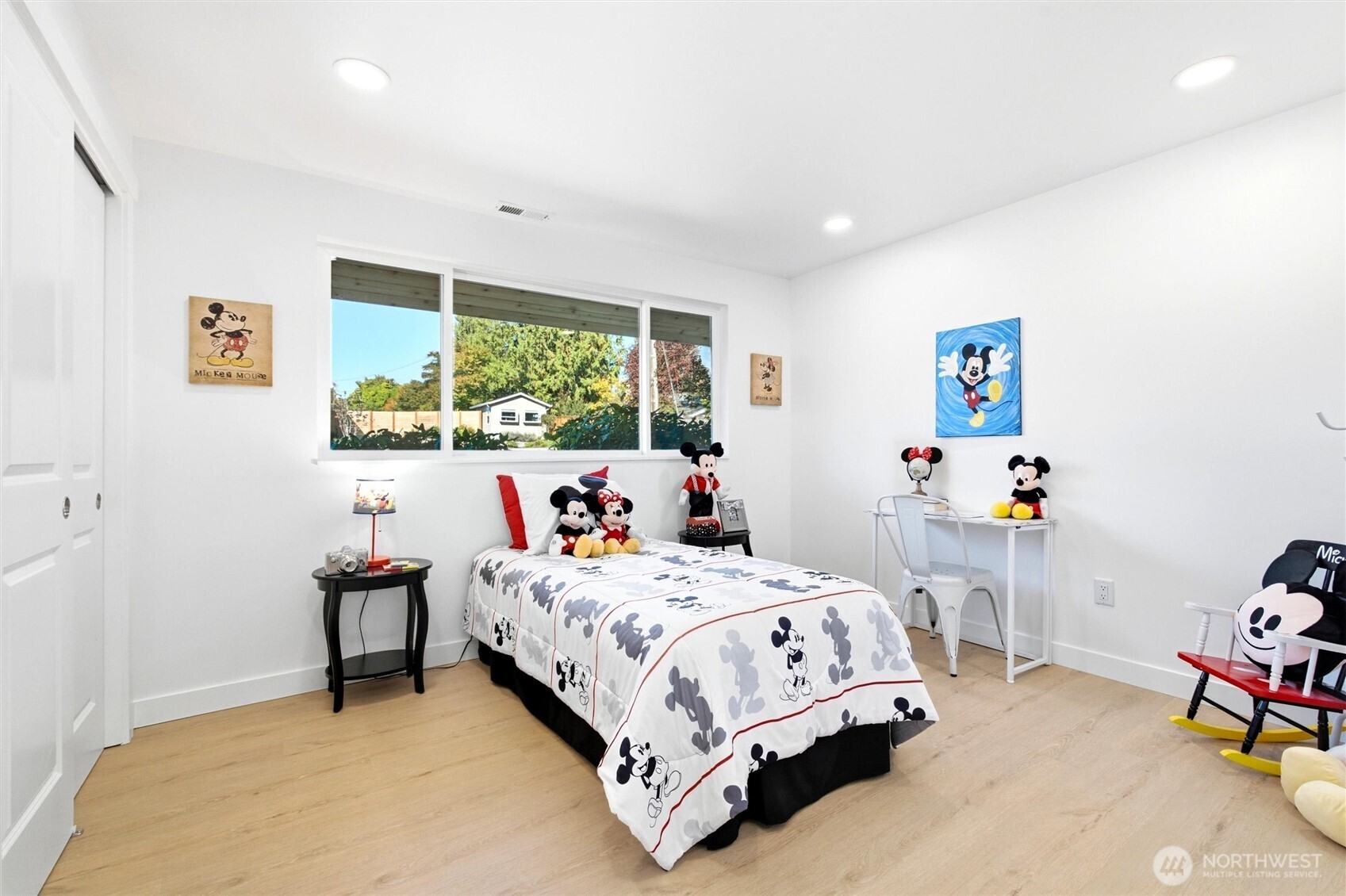 Bedroom with Mickey Mouse bedding and collectibles, light wood floors, and a wide window.