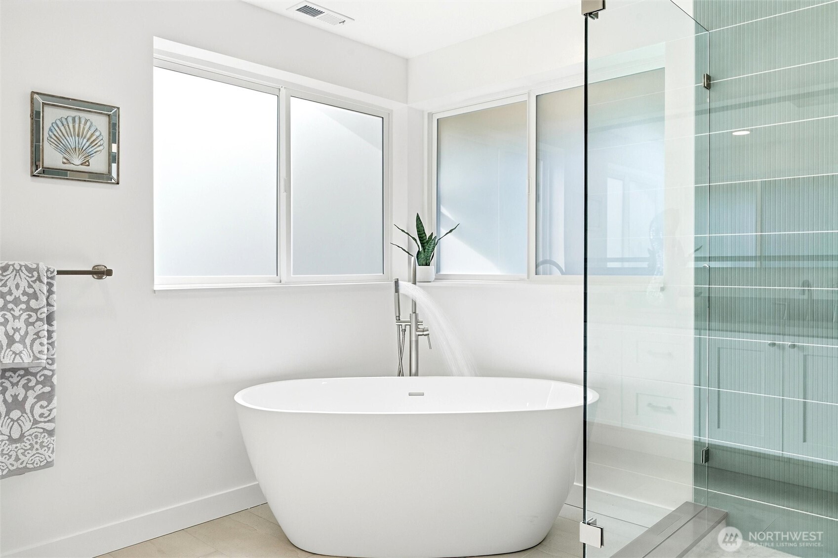Bright bathroom with a freestanding soaking tub beneath large windows beside a glass-enclosed shower.