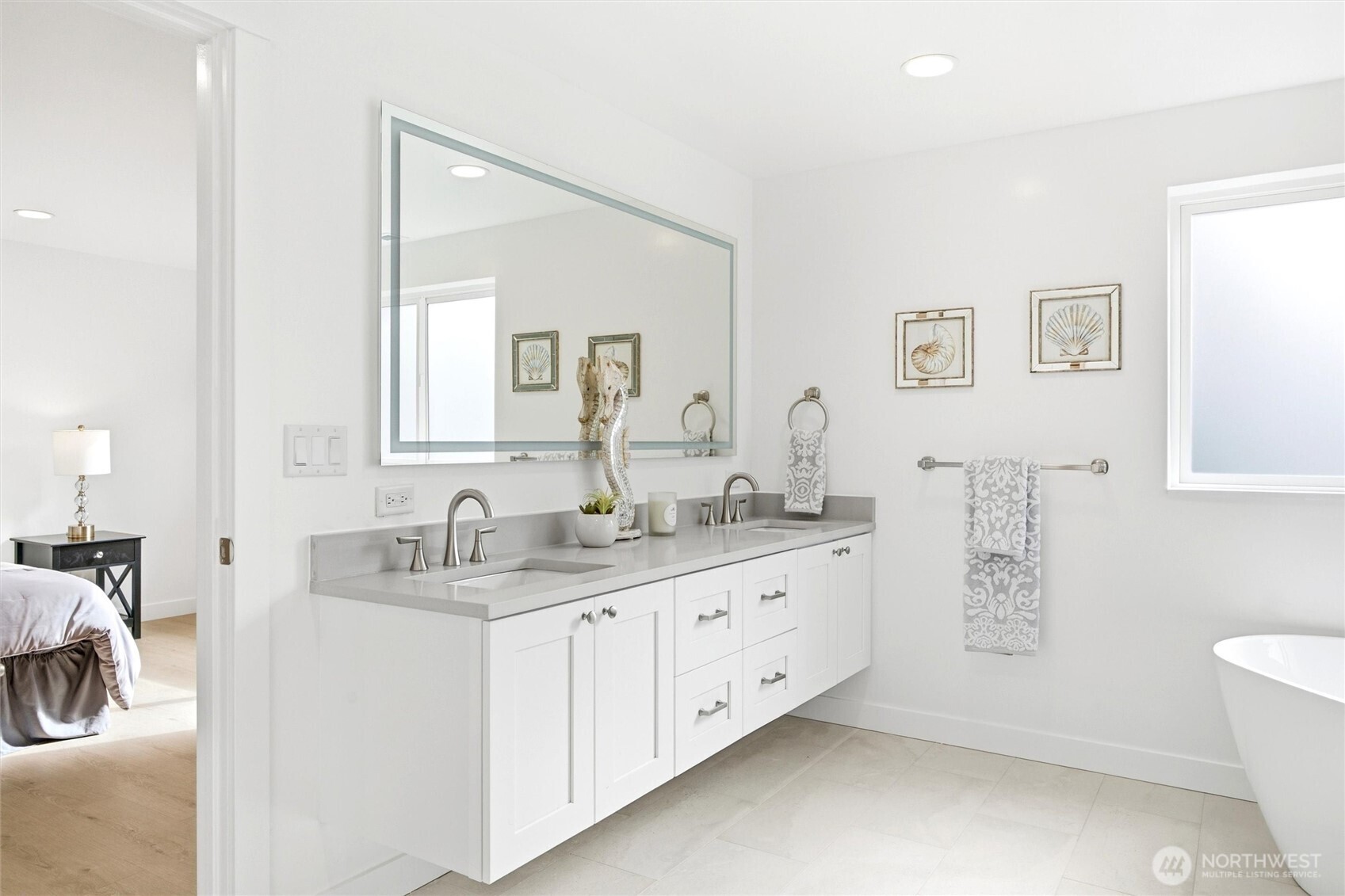 Bright bathroom with a long double vanity, large mirror, and freestanding tub.