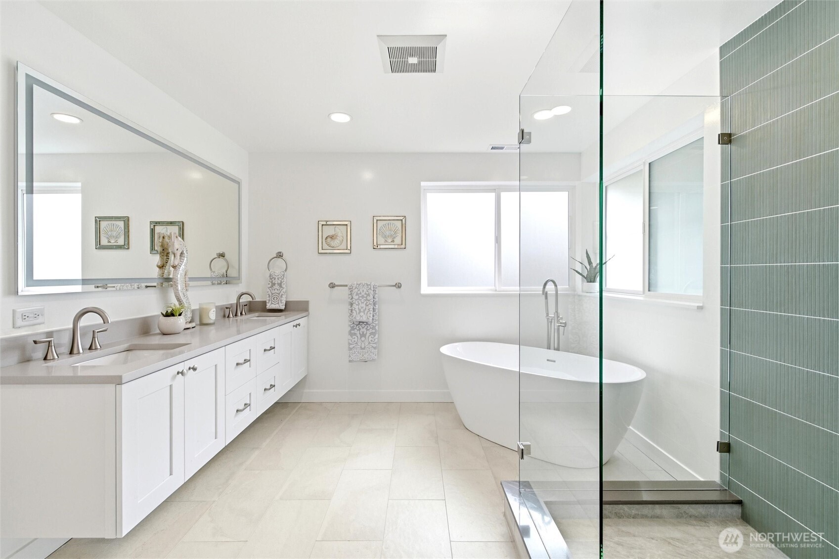 Bright bathroom with a long white vanity, freestanding soaking tub, and glass shower with green tile.