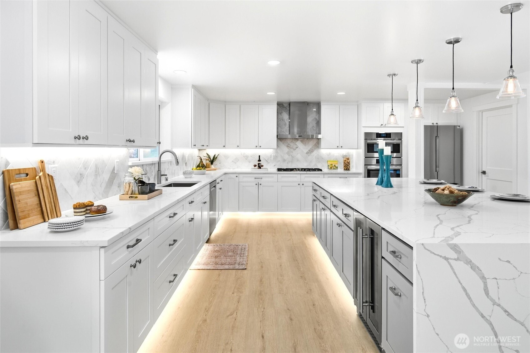 Bright white kitchen with a large marble-pattern island, stainless steel appliances, and light wood floors.