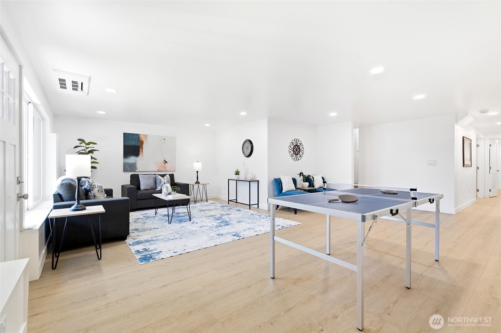 Furnished living room and game area with a blue ping-pong table, sofas, and large windows.