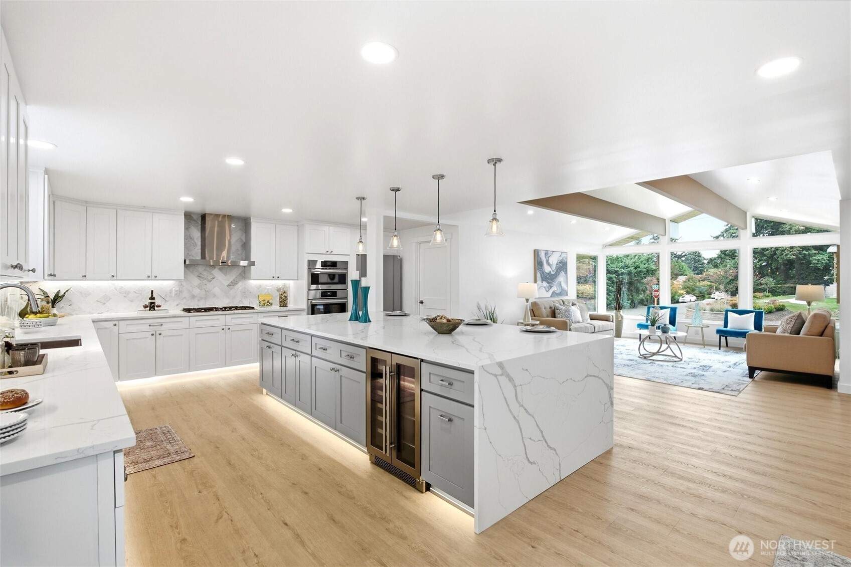 Bright kitchen with a large veined quartz island, white cabinetry, and windows overlooking the living room.