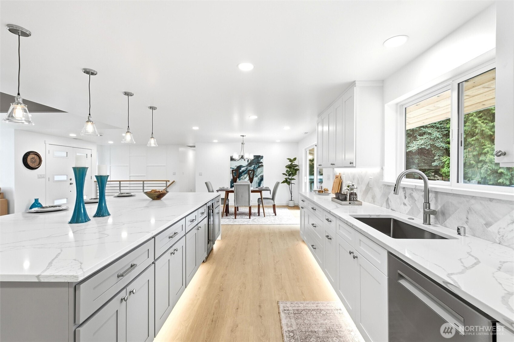 Bright white kitchen with a large island, marble-look counters, and dining area beyond.