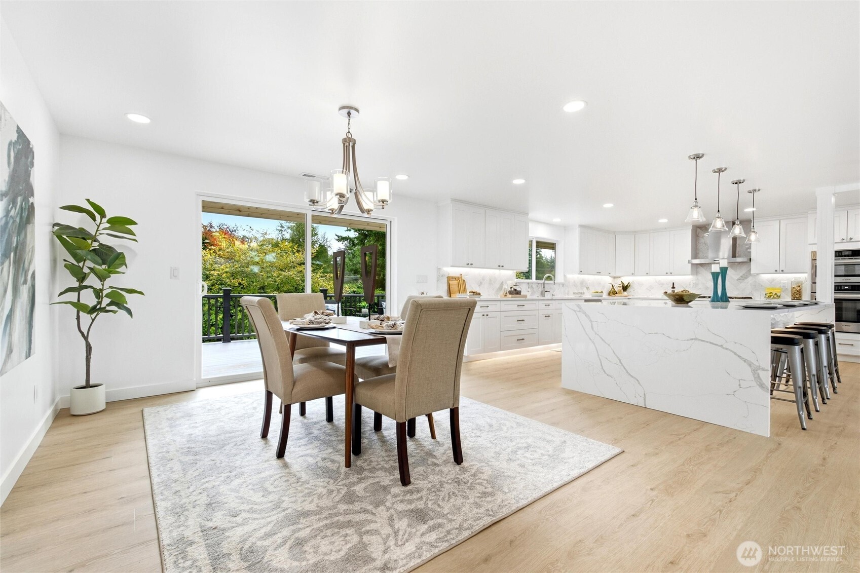 Open kitchen and dining area with a large veined quartz island and sliding doors to a deck.