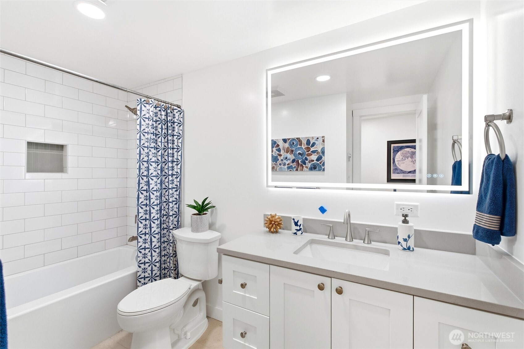 Bright bathroom with a subway-tile tub surround, patterned blue shower curtain, and white vanity.