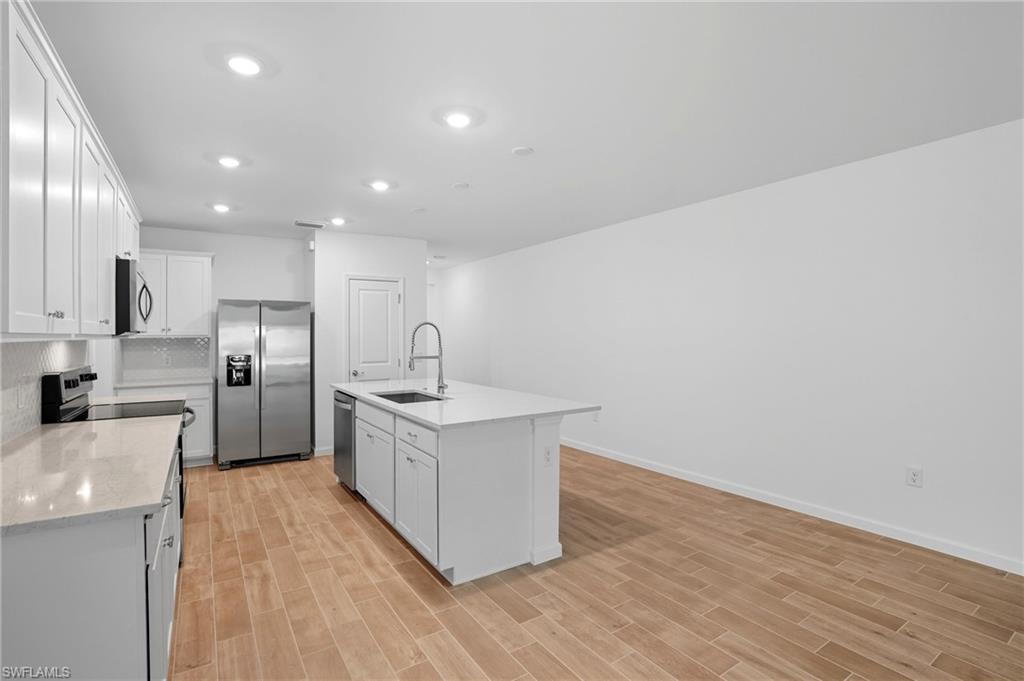 Kitchen with white cabinets, stainless steel appliances, a large island, and light wood-look tile flooring.