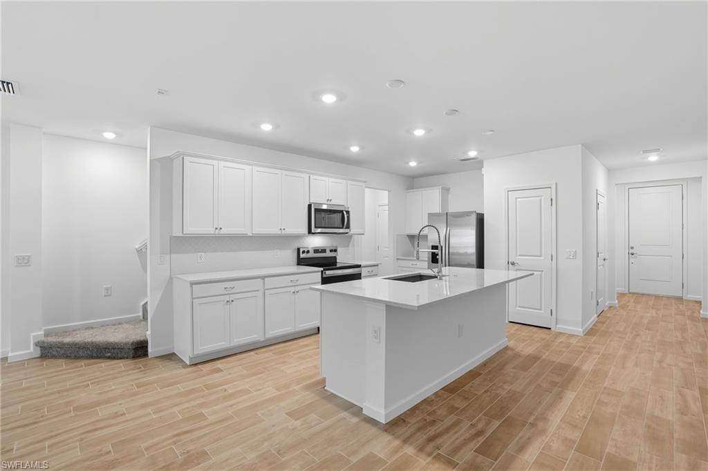Kitchen with a large sink island, white cabinets, stainless steel appliances, and wood-look tile flooring.