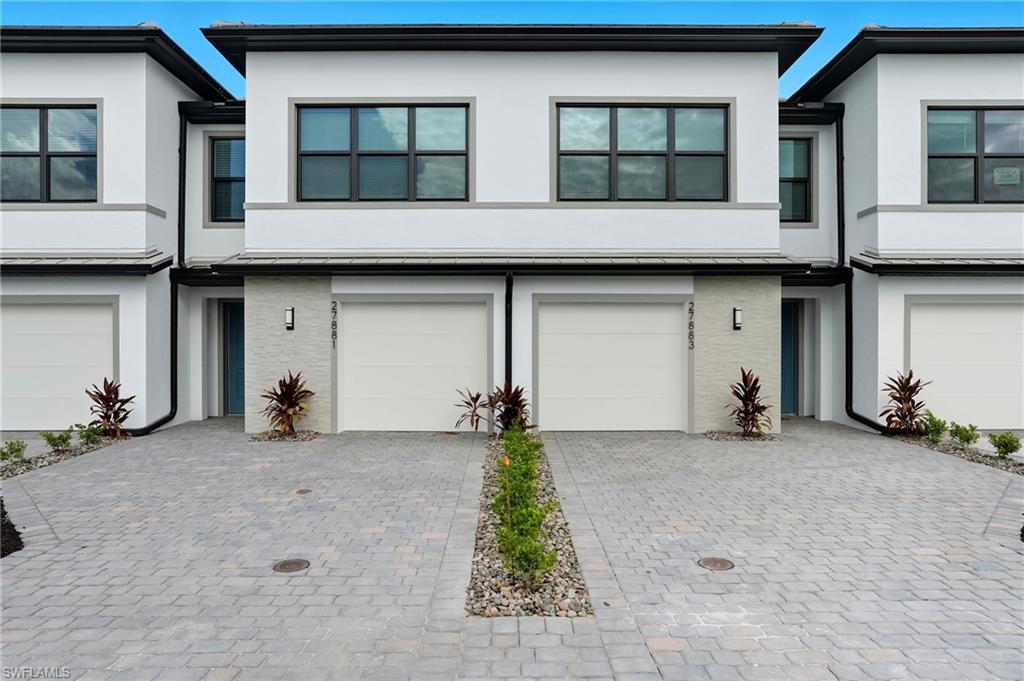 Modern two-story townhome with white exterior, black trim, garage, and paver driveway.