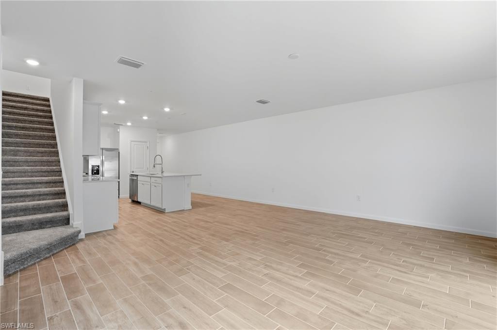 Unfurnished open living area with wood-look tile floors, a kitchen island, and carpeted stairs.