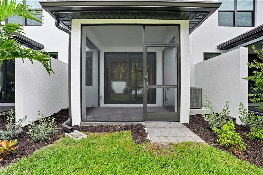 Screened lanai with black-framed doors, paver walkway, and landscaped lawn.