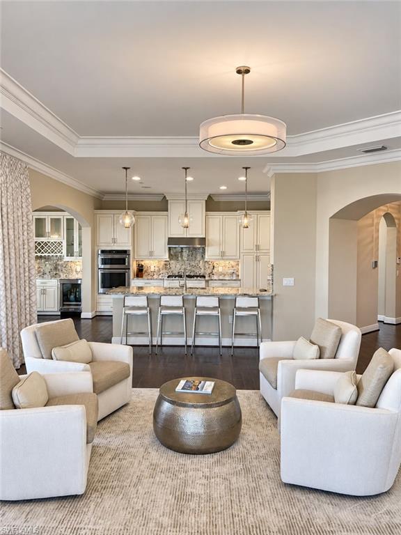 Living room with cream armchairs and a round metallic coffee table, opening to a white kitchen.