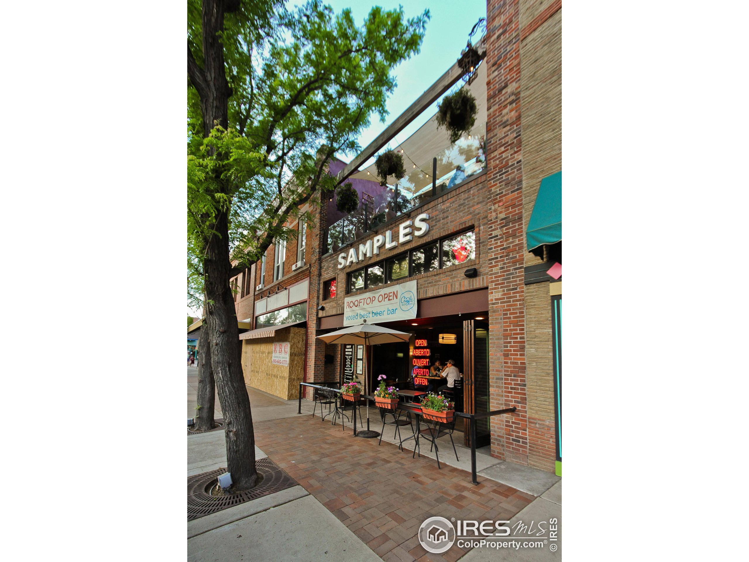 Brick restaurant storefront with outdoor tables, flower boxes, and a rooftop patio.