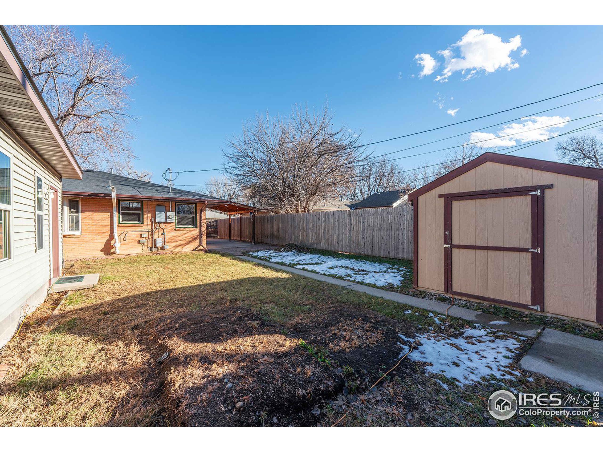 Fenced backyard with a detached shed, concrete walkway, and patches of snow.