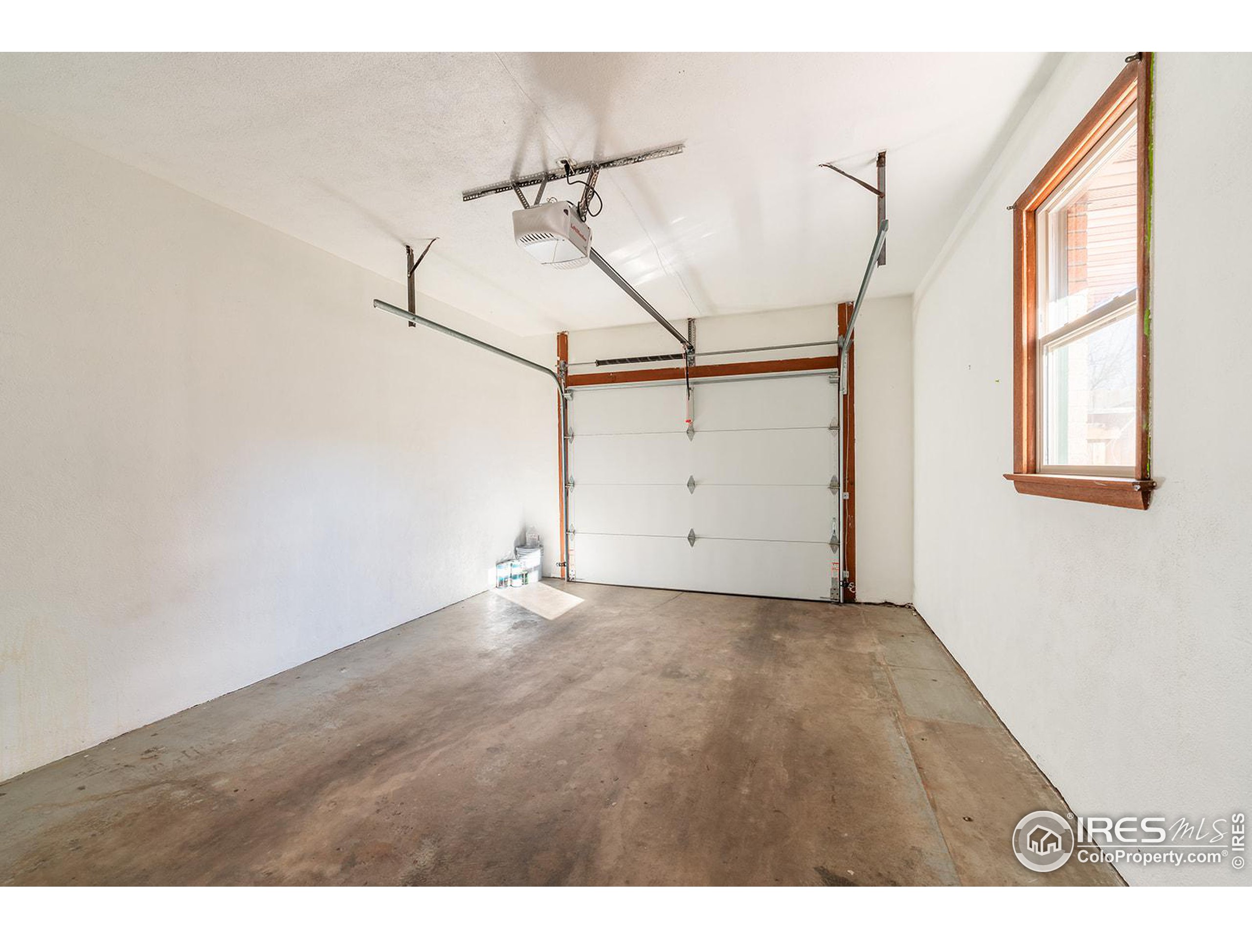 Empty garage with a concrete floor, closed overhead door, and wood-trimmed window.