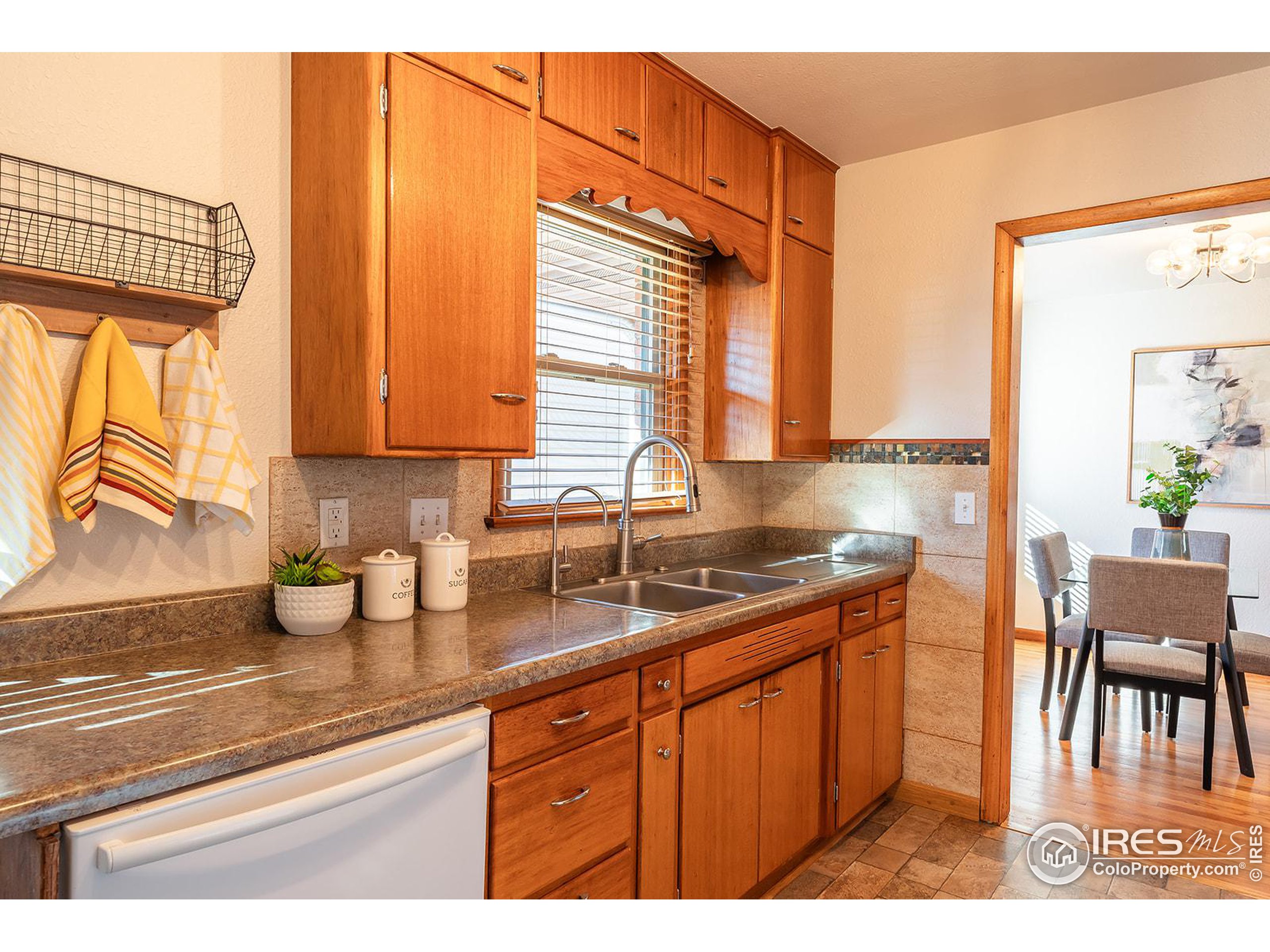 Kitchen with warm wood cabinets, double sink under a window, and doorway to the dining area.