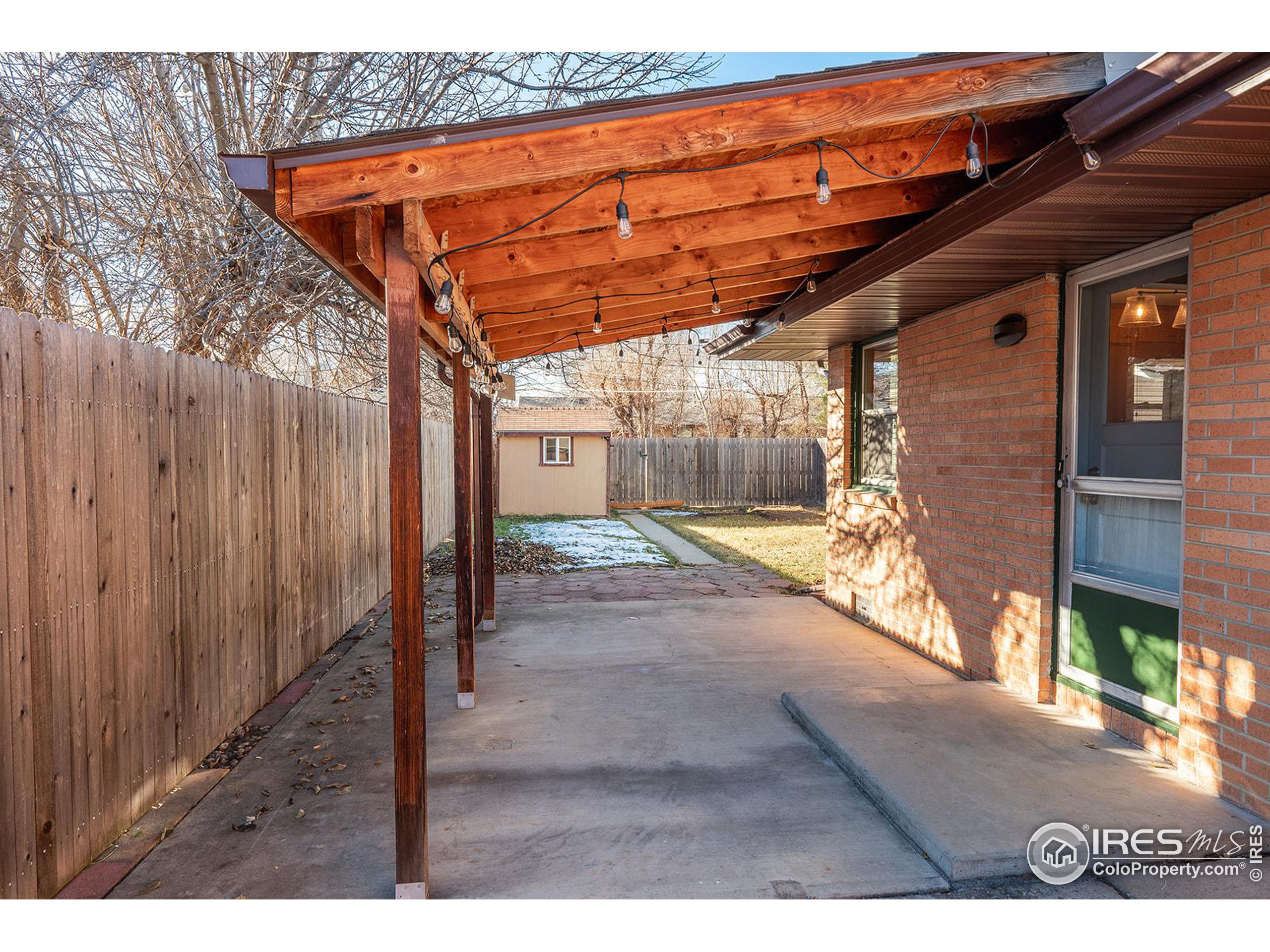 Covered backyard patio with a timber roof, string lights, brick wall, and fenced yard.