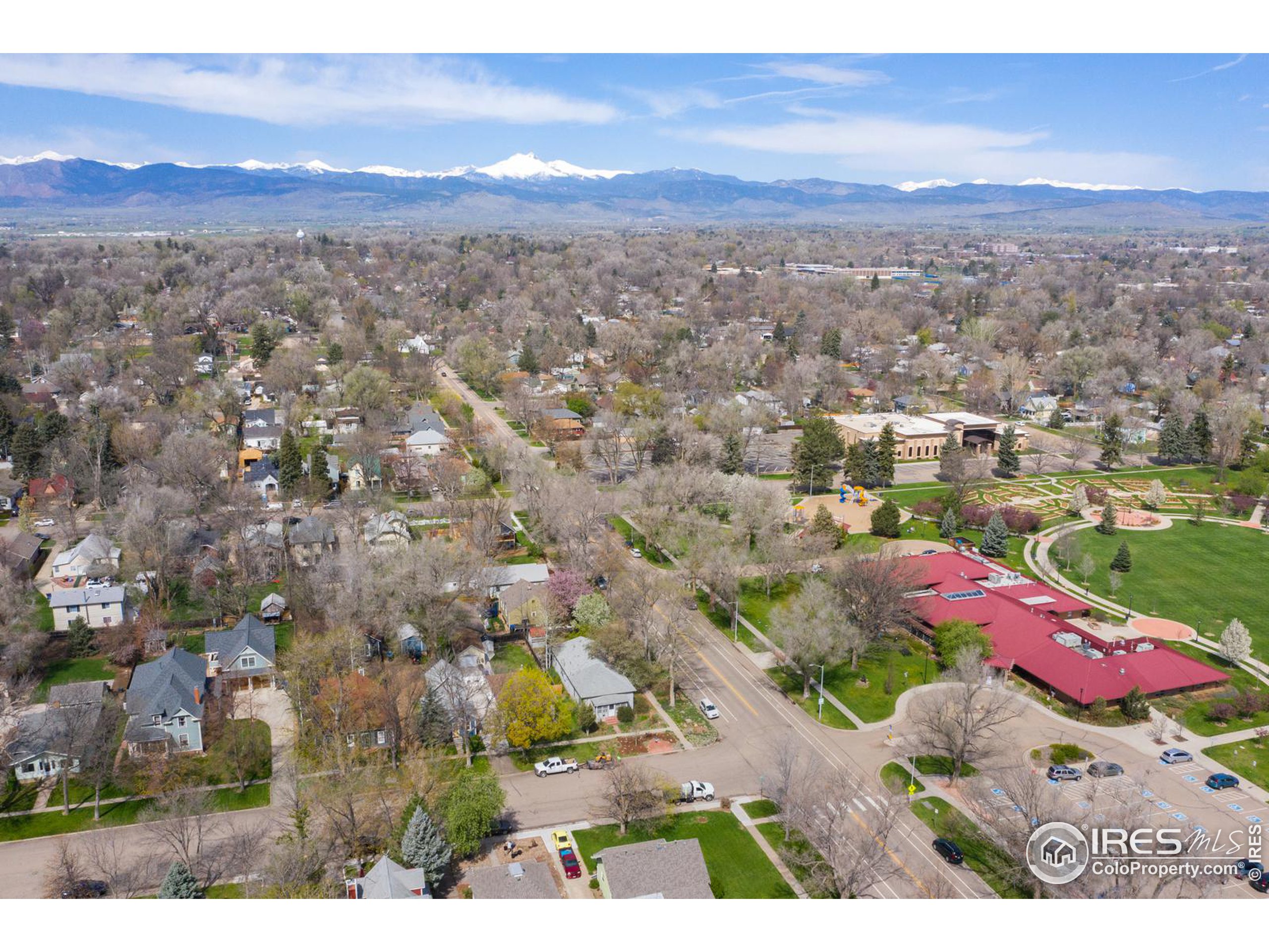 Aerial view of a Longmont neighborhood and park, with snow-capped mountains on the horizon.