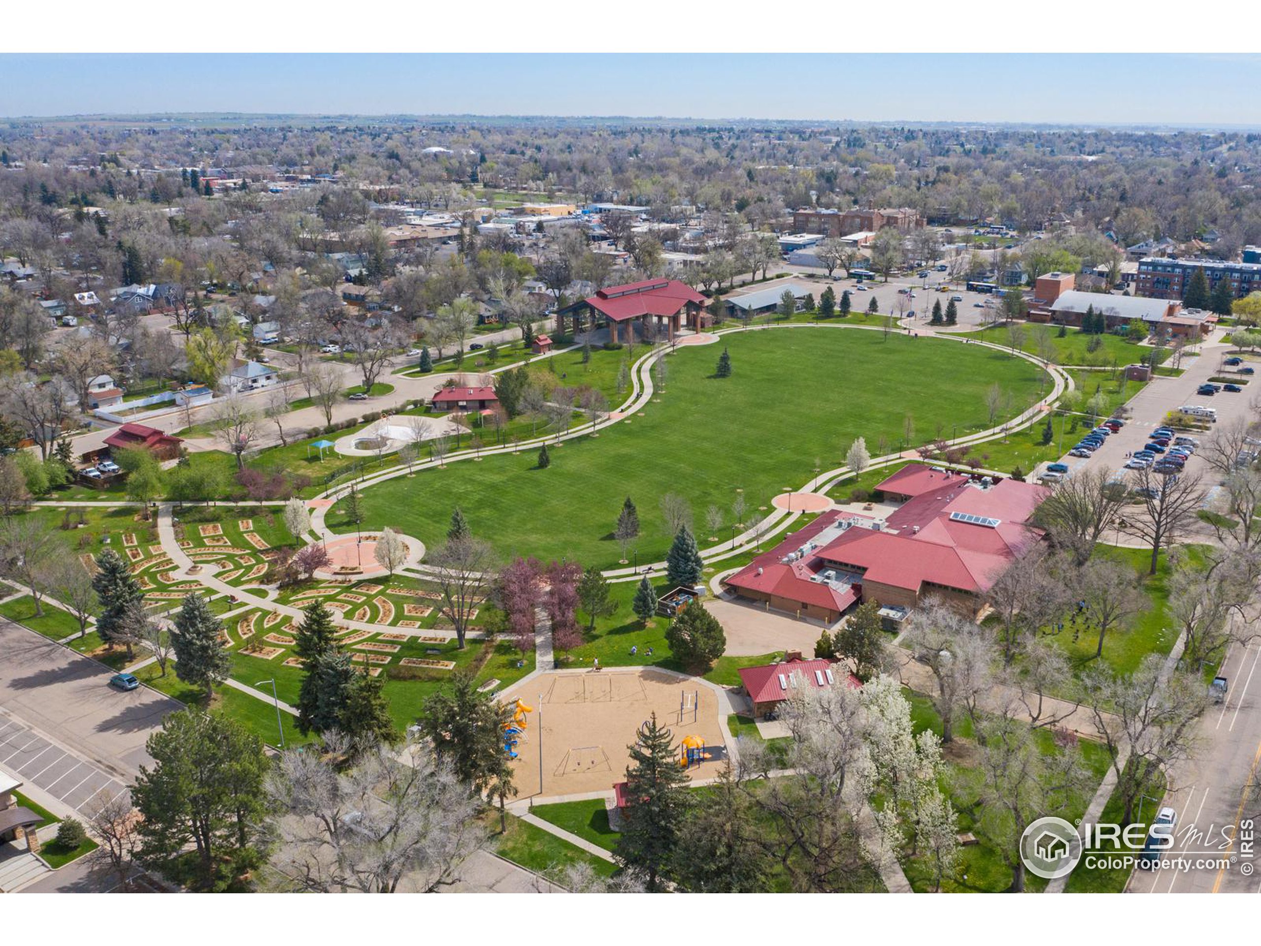 Aerial view of a neighborhood park with a large lawn, winding paths, gardens, and a playground.