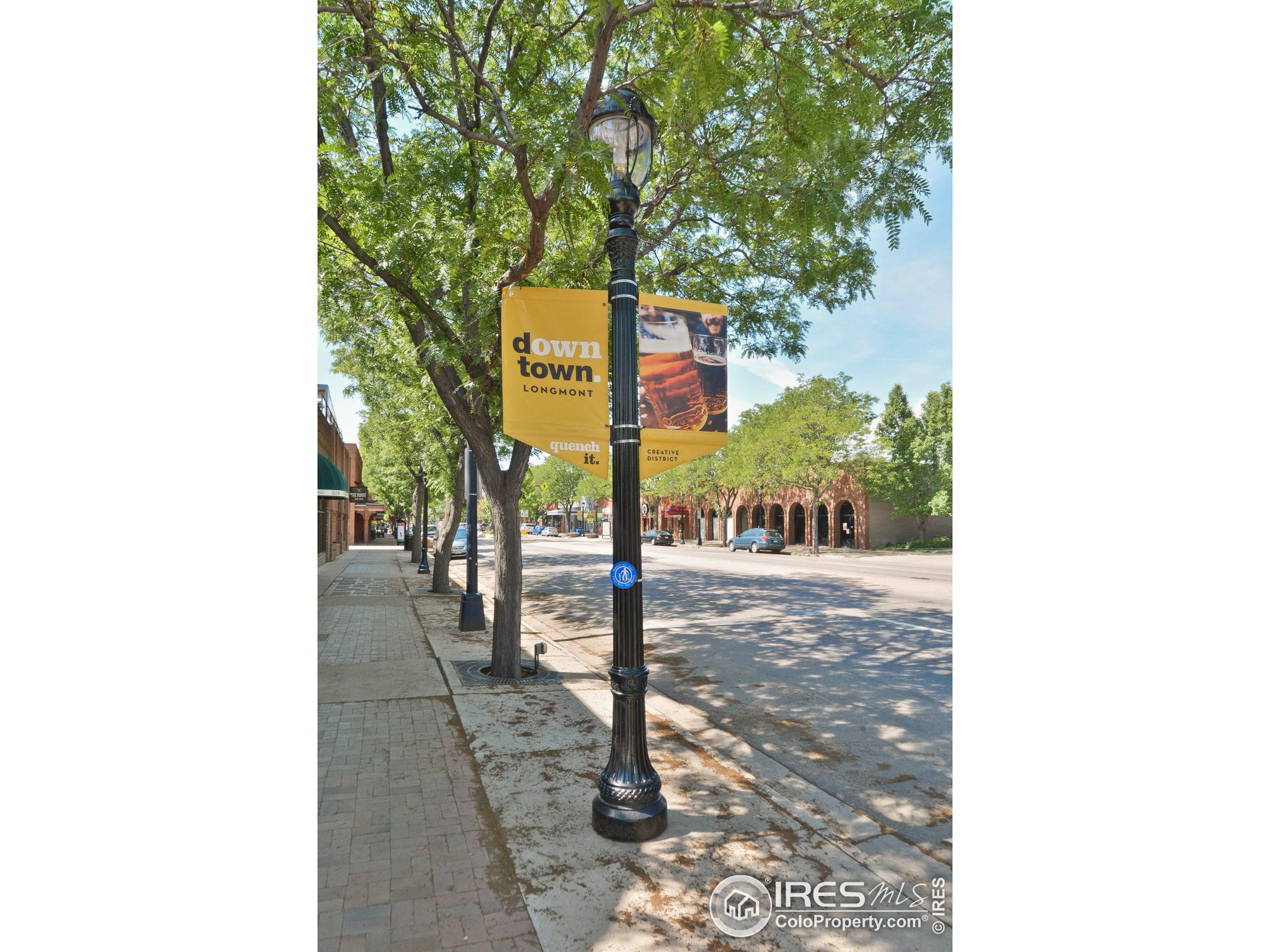 Tree-lined downtown Longmont street with brick storefronts and yellow downtown banners.