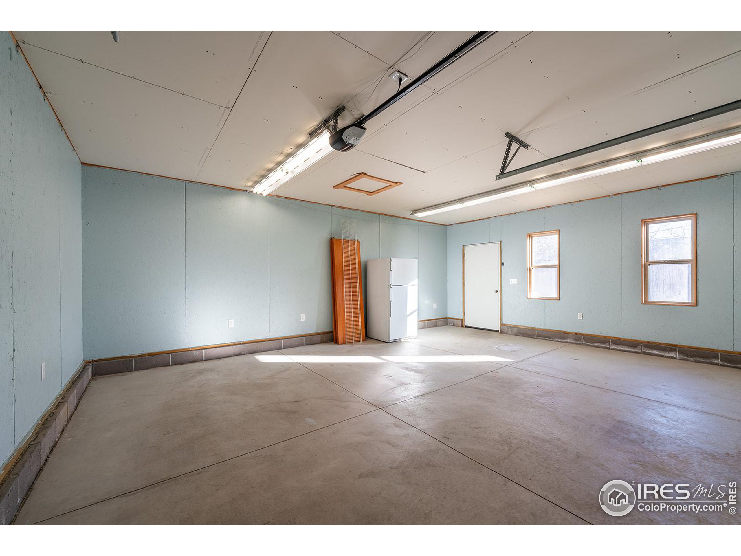 Vacant garage with a concrete floor, pale blue walls, fluorescent lights, and two windows.