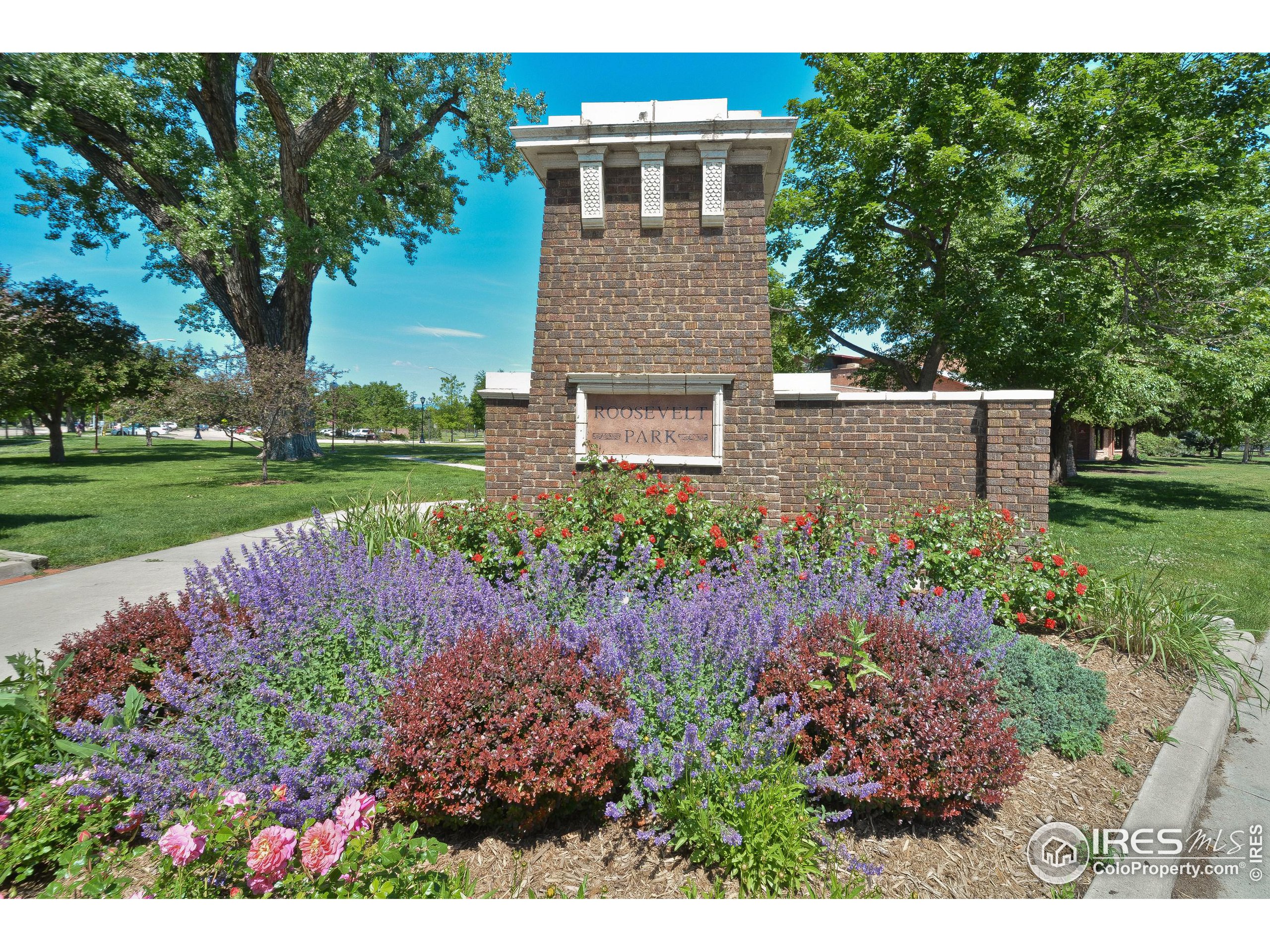 Roosevelt Park entrance sign behind flower beds and mature trees.