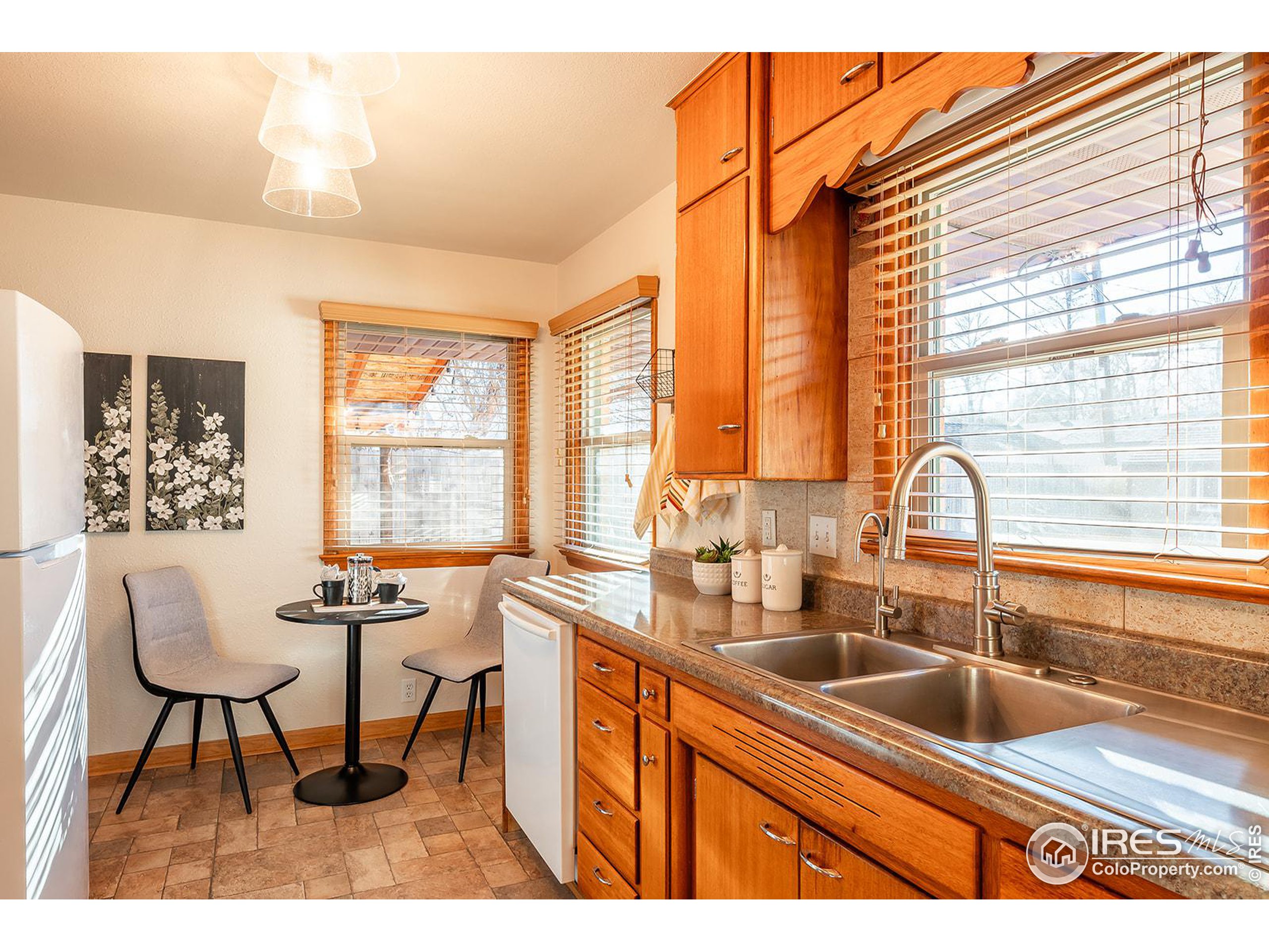 Kitchen with warm wood cabinets, a double-basin sink, and a small dining nook beside large windows.
