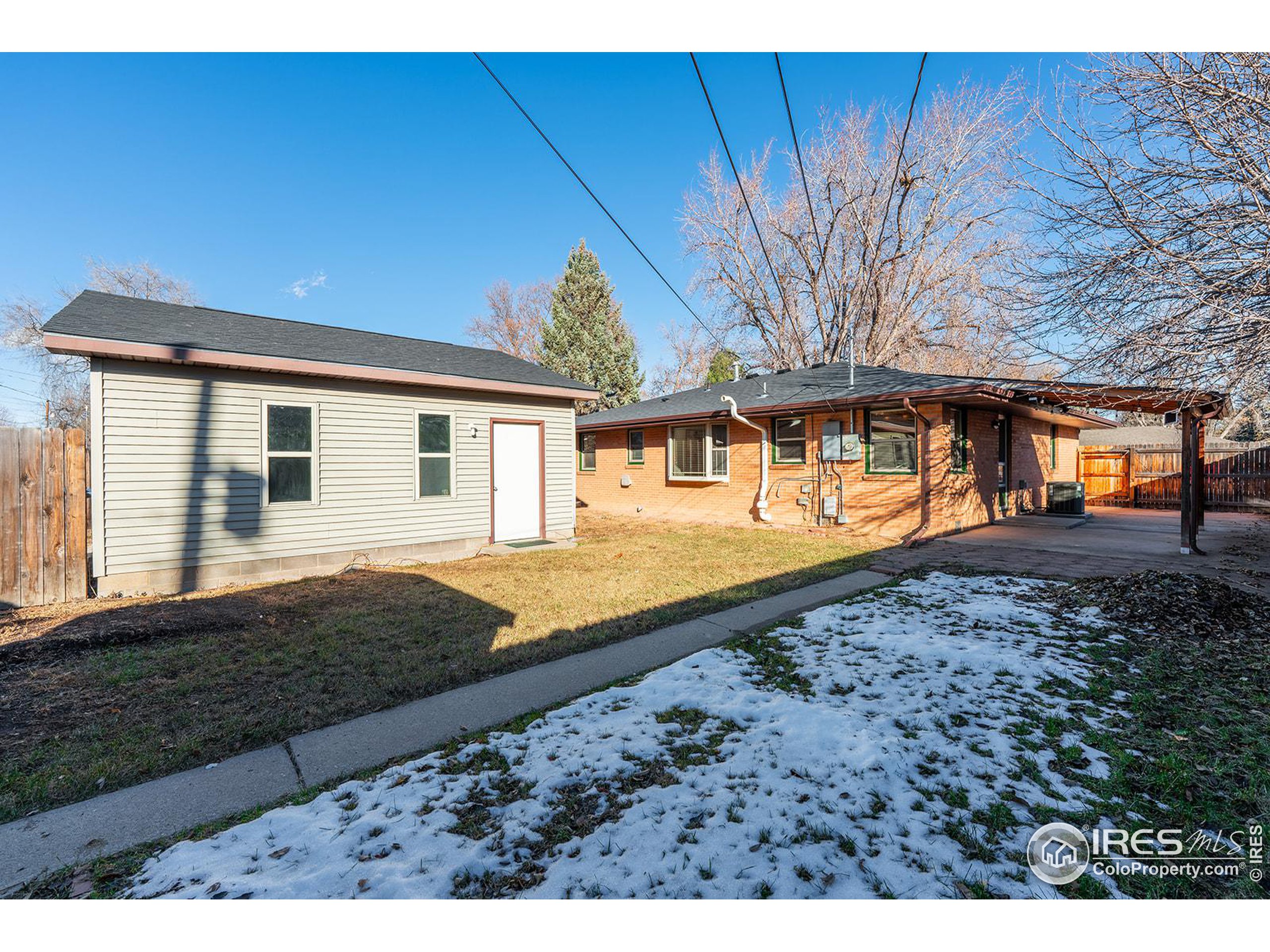 Rear of a brick home with a covered carport, detached outbuilding, and snow-patched yard.