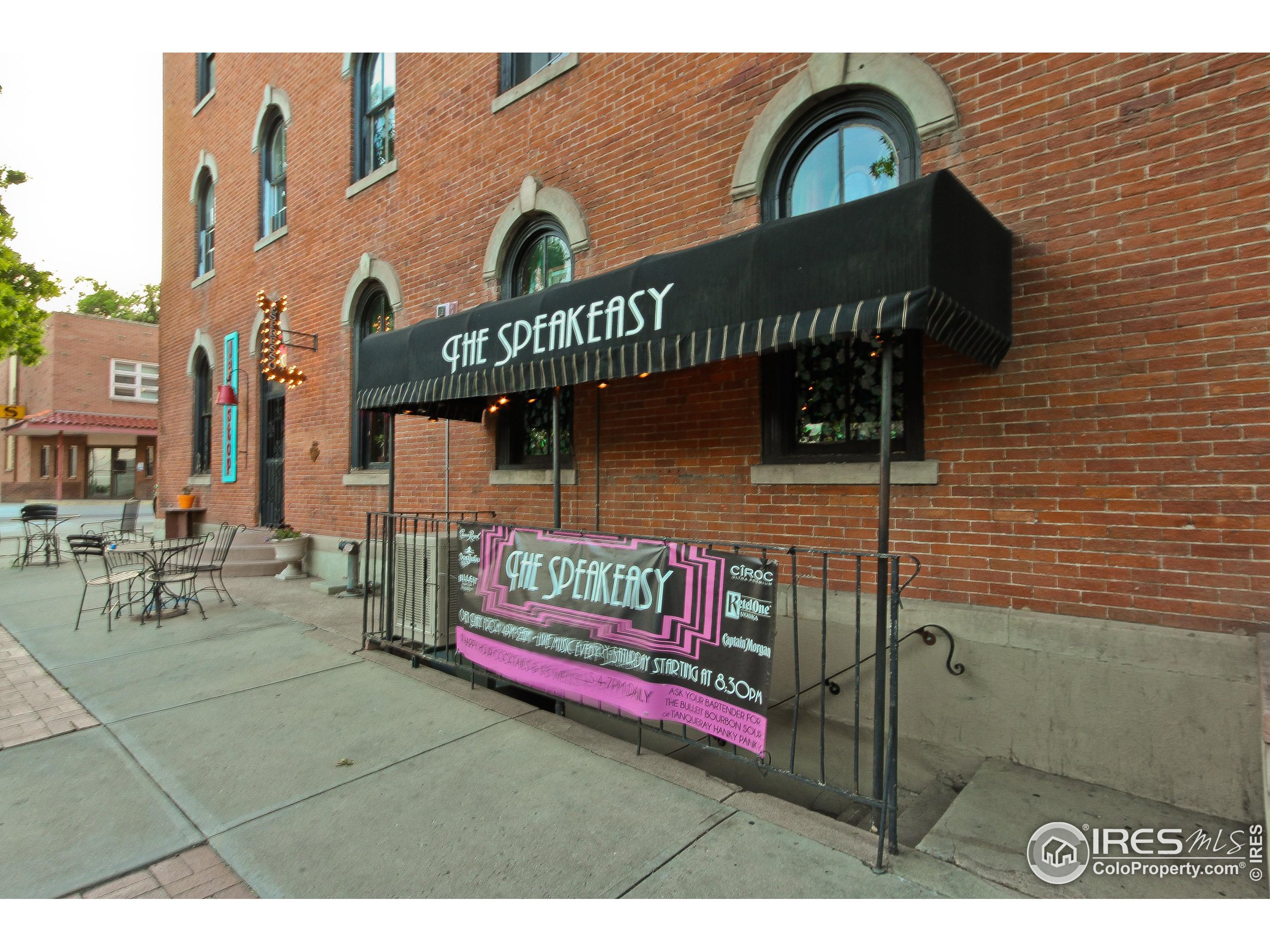 Brick storefront with arched windows, a black Speakeasy awning, and sidewalk patio seating.