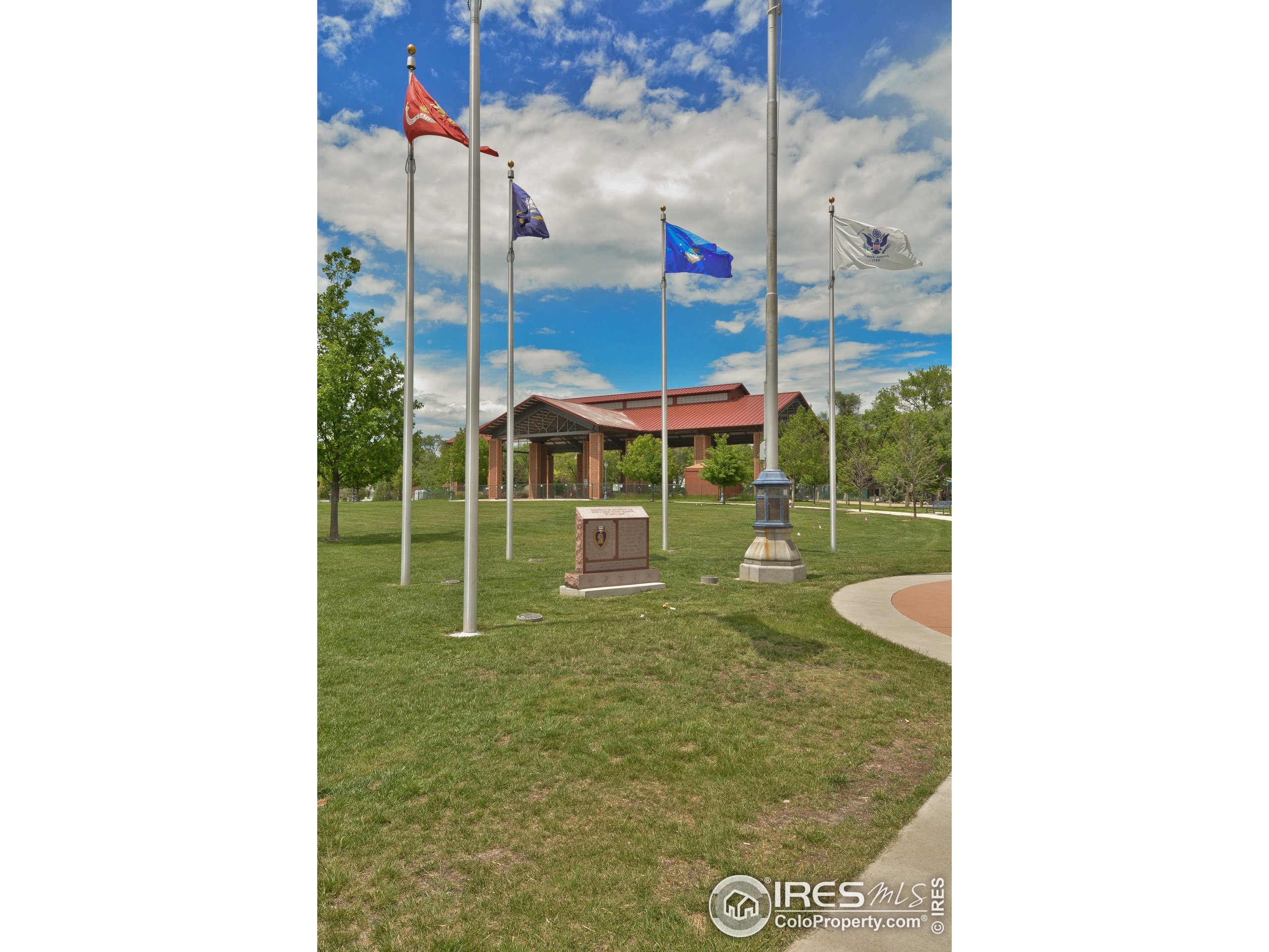 Park lawn with flags, a stone memorial, and a brick pavilion with a red roof.