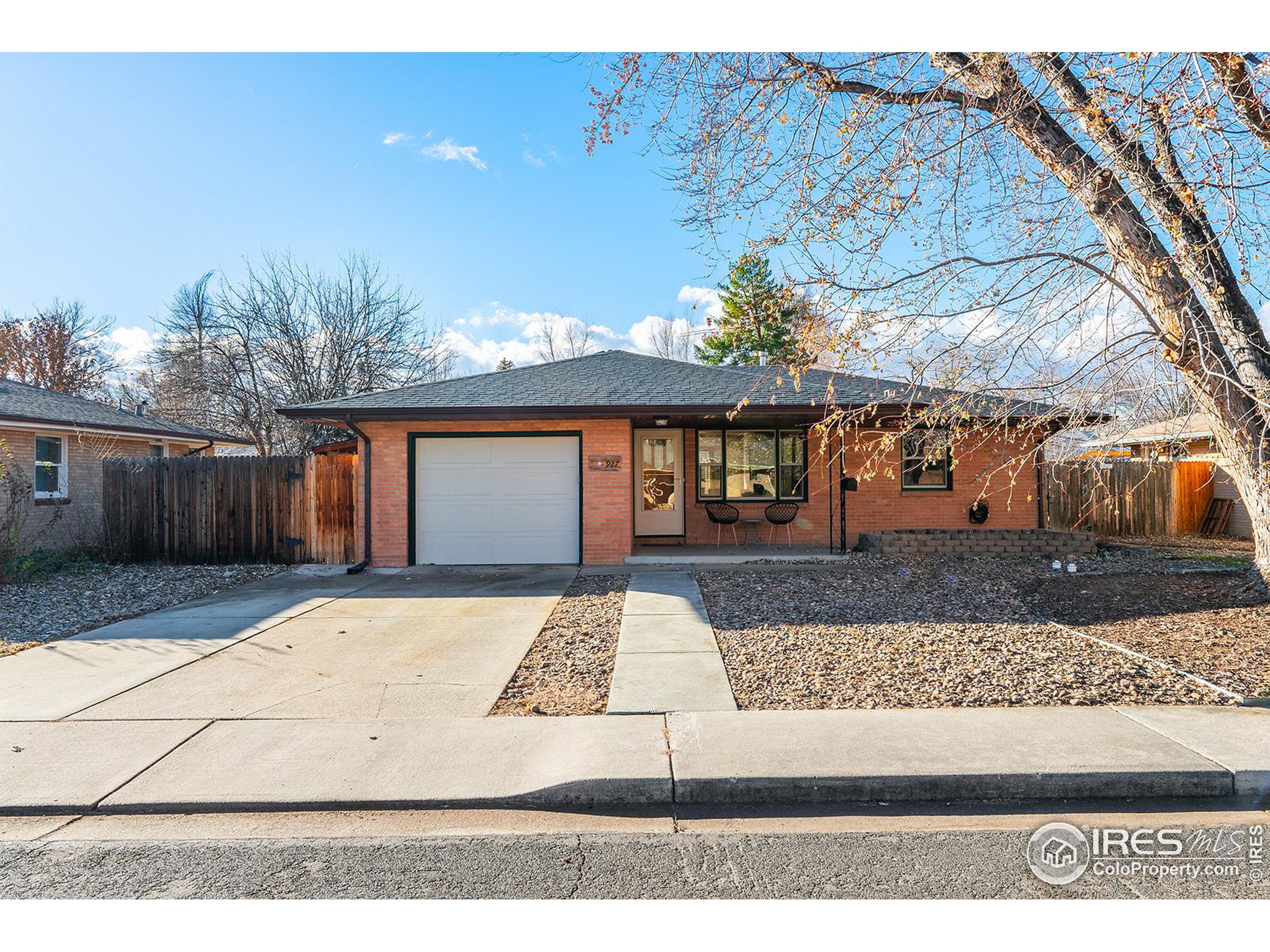 Single-story brick home with an attached garage, concrete driveway, and mature trees.