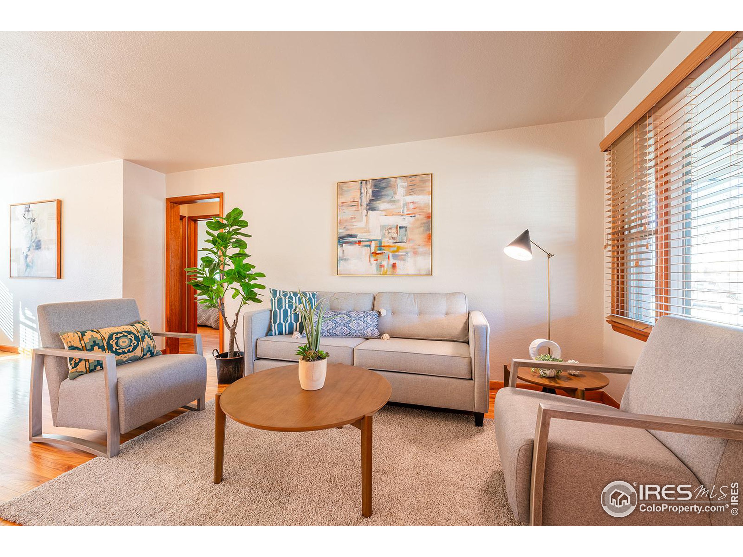 Bright staged living room with gray seating, a round wood coffee table, and a large window.