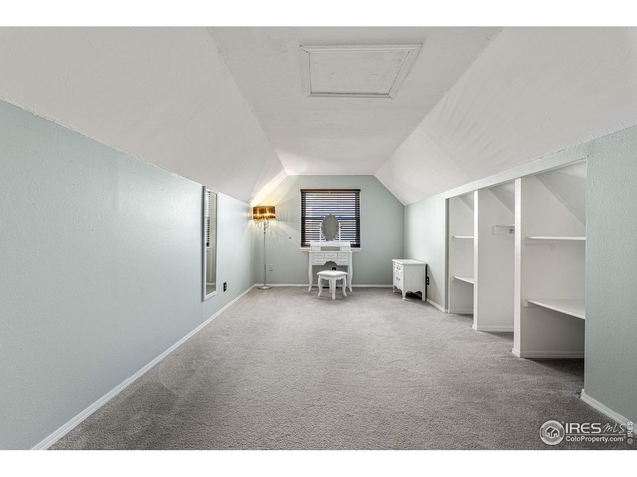 Attic bedroom with a white vanity beneath the window and open built-in shelving along one side.