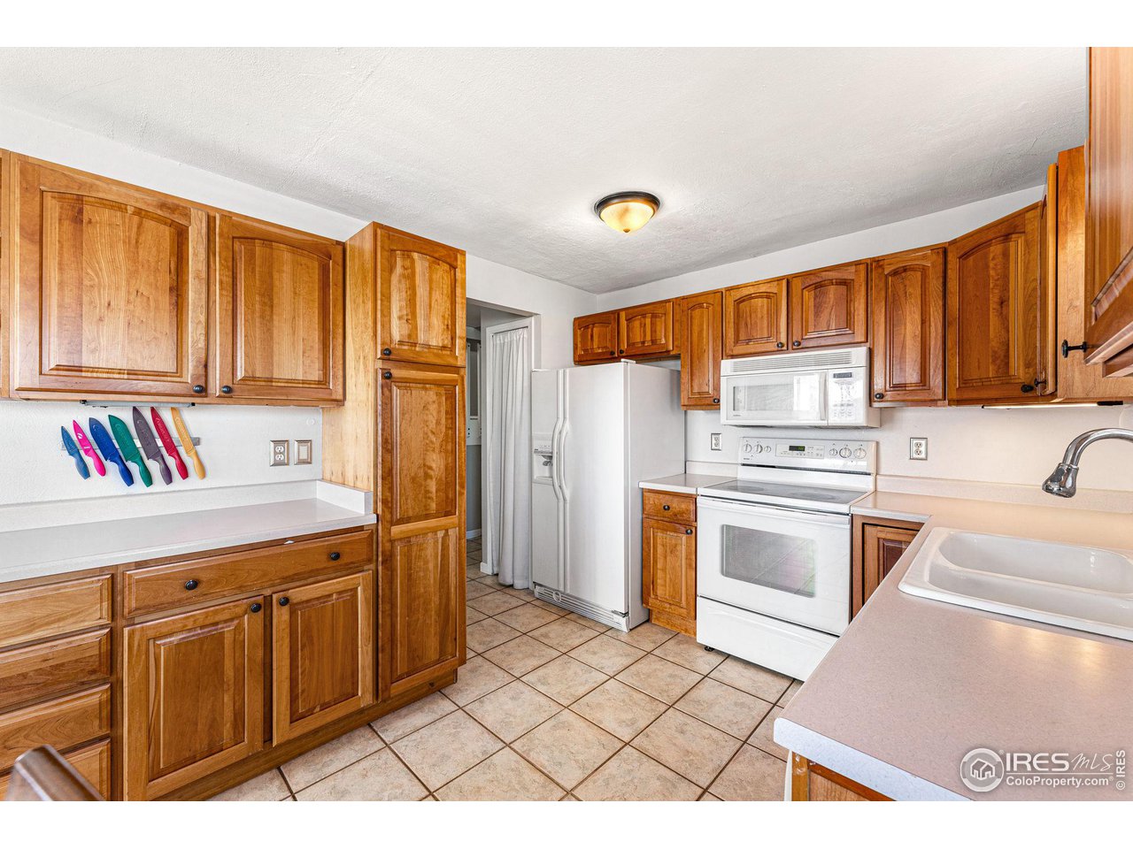 Kitchen with honey-colored wood cabinets, white appliances, and a tiled floor.