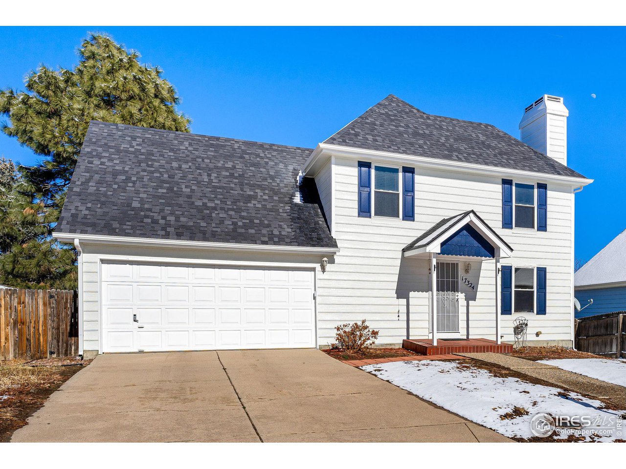Two-story white house with blue shutters, a large garage, and snow patches on the lawn.