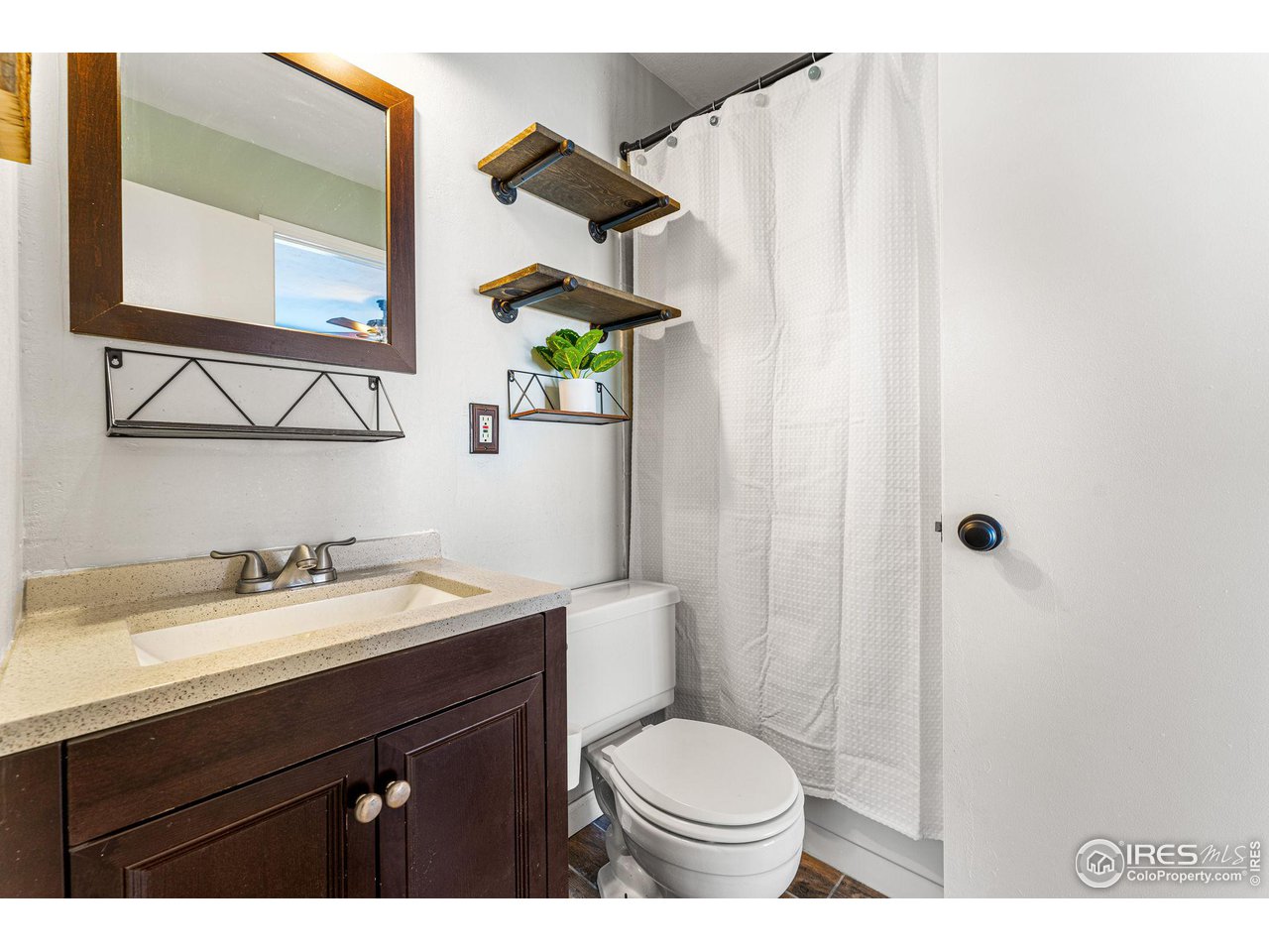 Bathroom with dark wood vanity, white tub and shower curtain, toilet, and floating wall shelves.